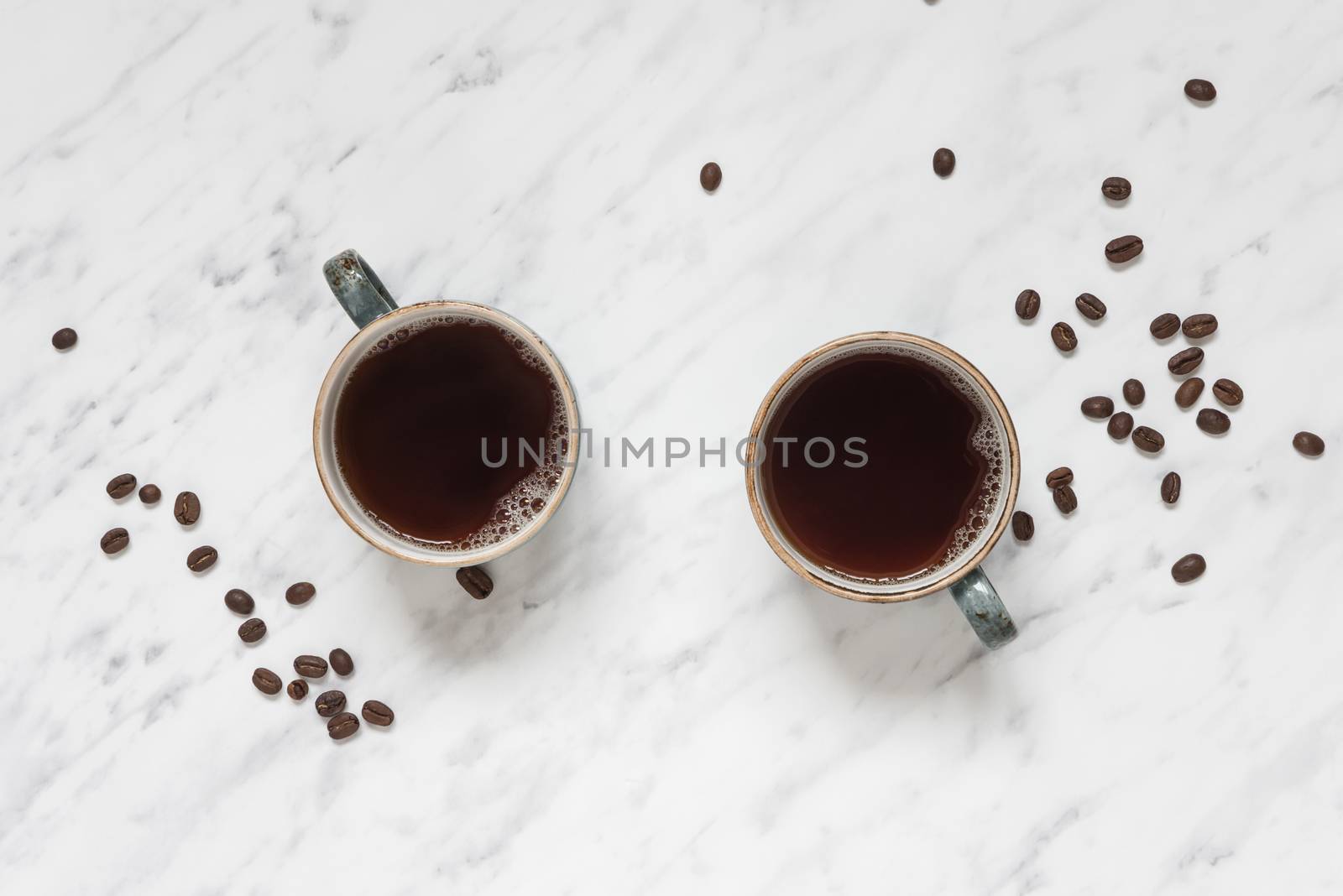 Morning composition with two cups of black coffee and coffee beans on a marble surface with space for text, top view