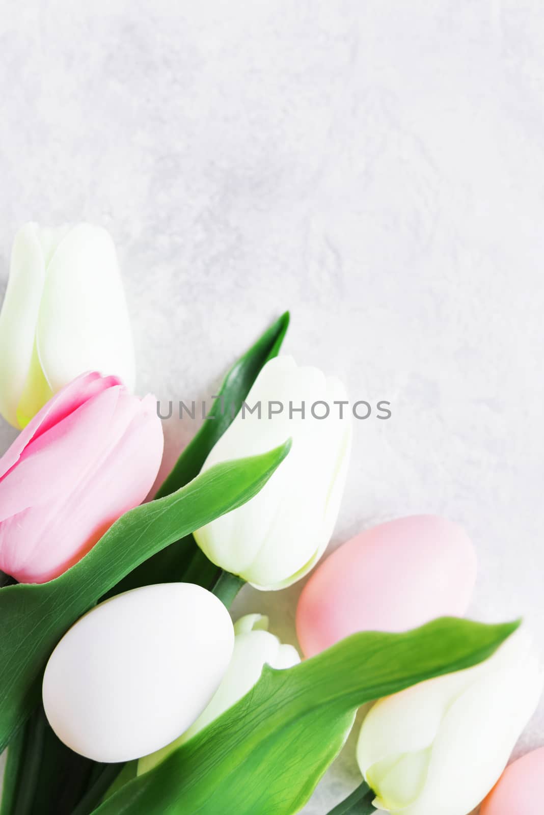Easter composition with a bouquet of pink and white tulips and Easter eggs on the background of stone surface, with copy-space