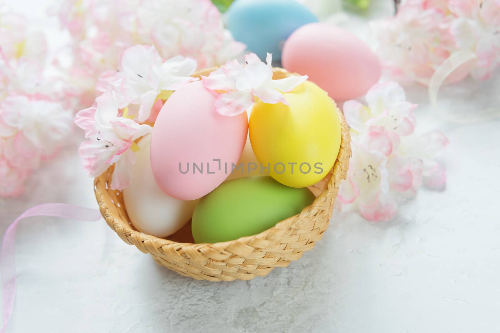 Easter composition with multicolored easter eggs in a wicker basket on the background of delicate pink flowers of the cherry blossoms