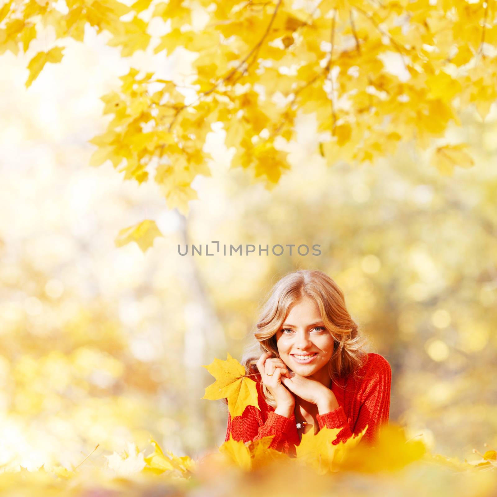 Beautiful young woman laying on yellow leaves in autumn park