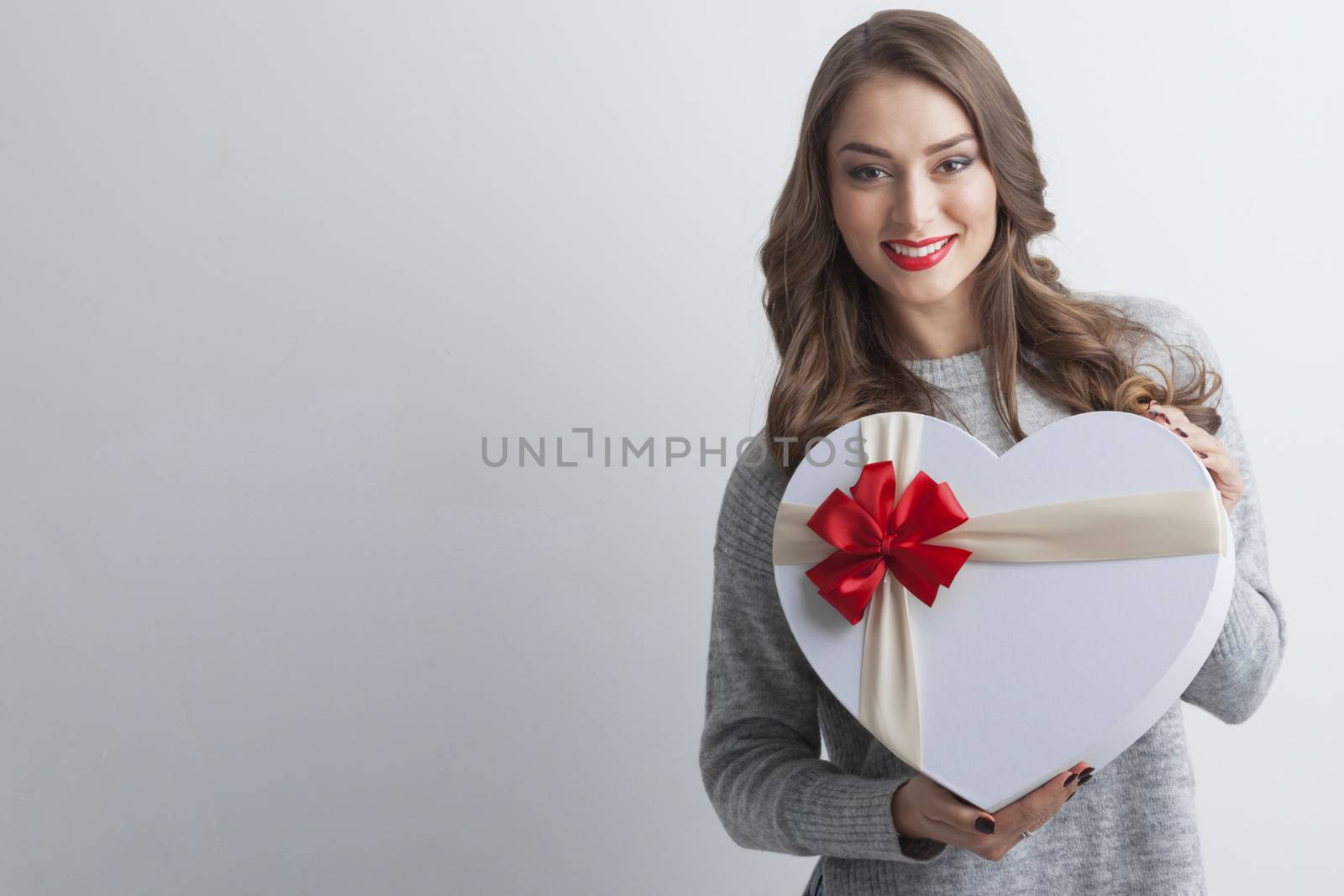 Young girl with heart-shaped gift box on white background