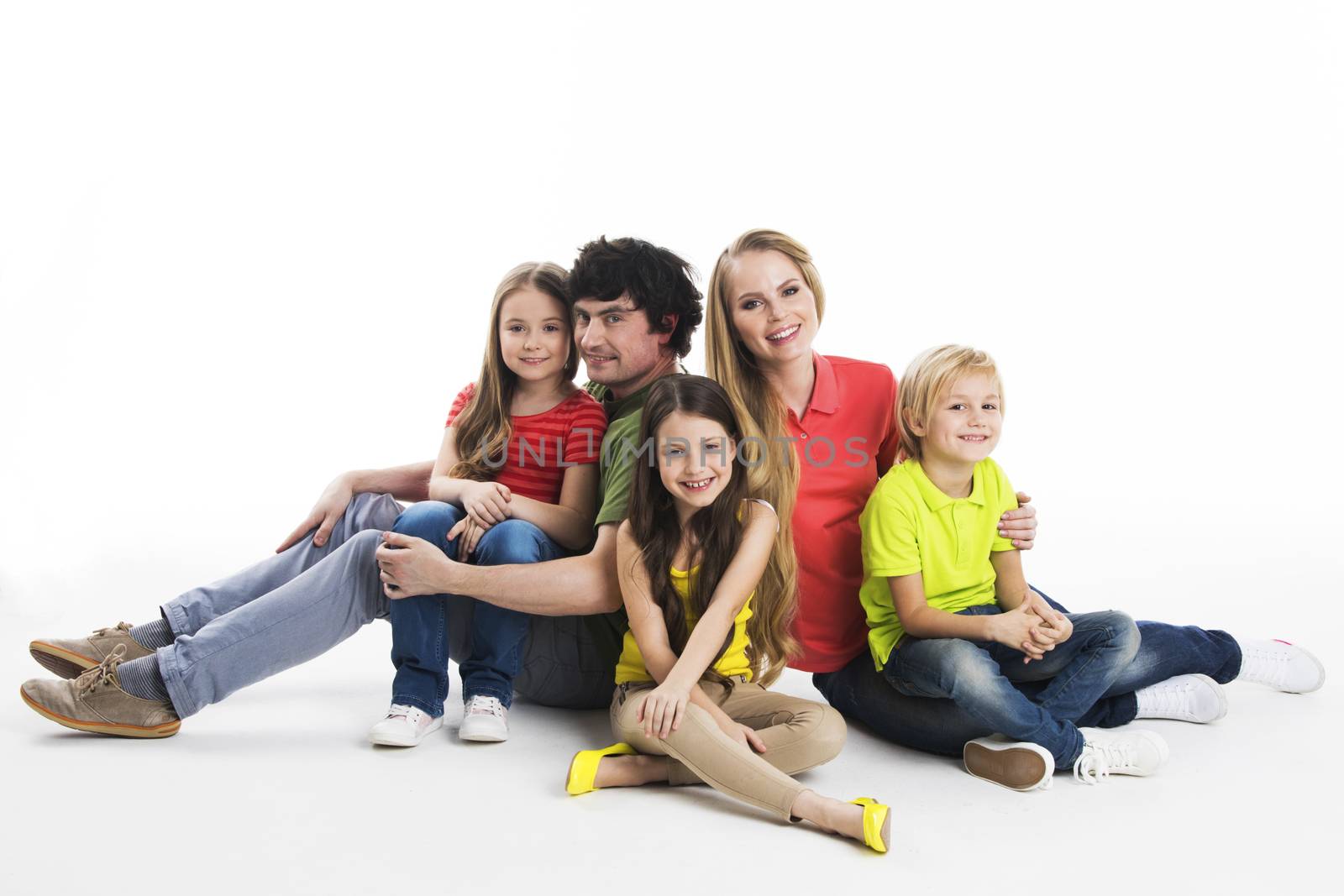 Portrait of happy family with three children sitting on the floor at studio isolated on white background