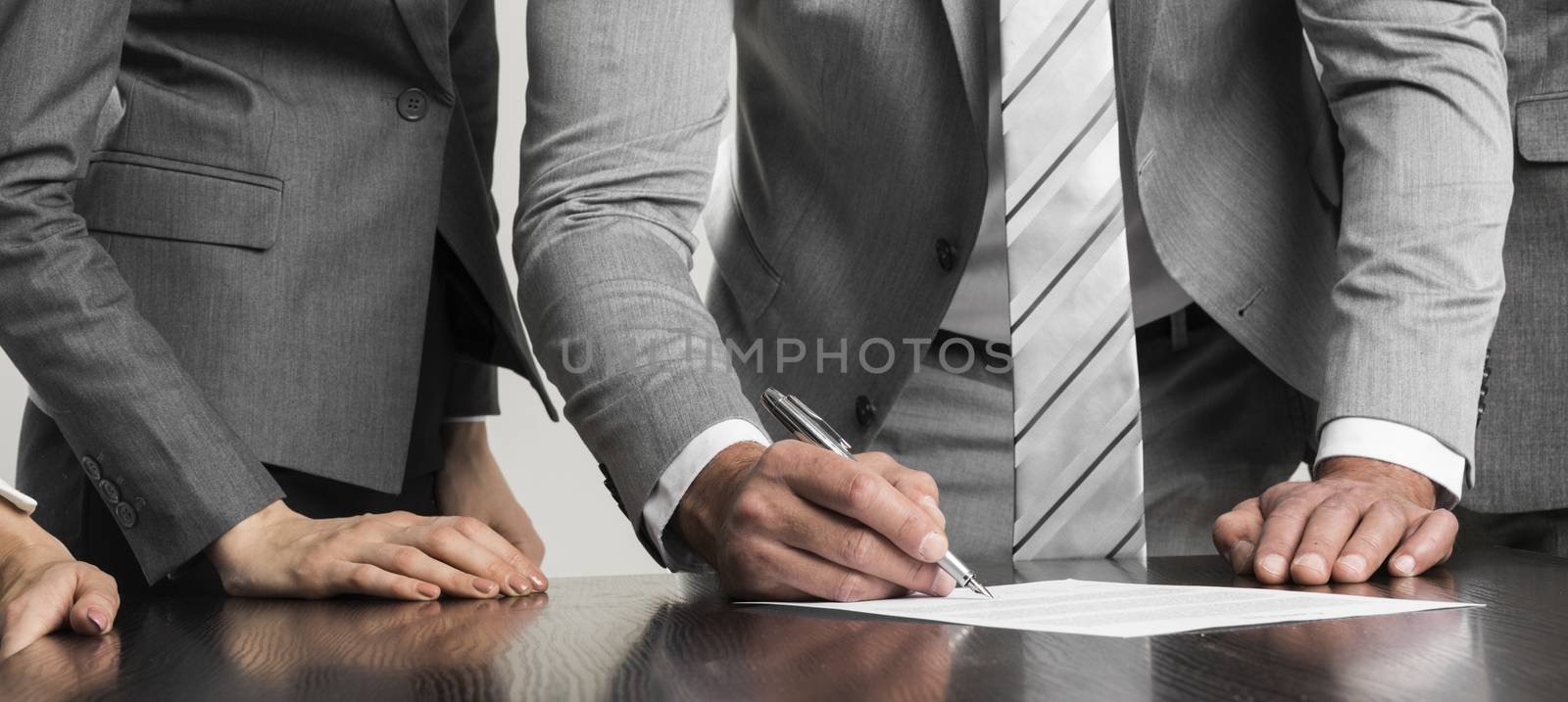 Businessman signing contract while his team is looking at him