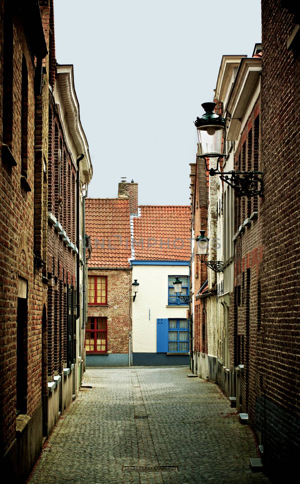 Obsolete Narrow Street with Multi Colored Old Houses and Street Lantern in Cloudy Day Outdoors. Bruges, Belgium