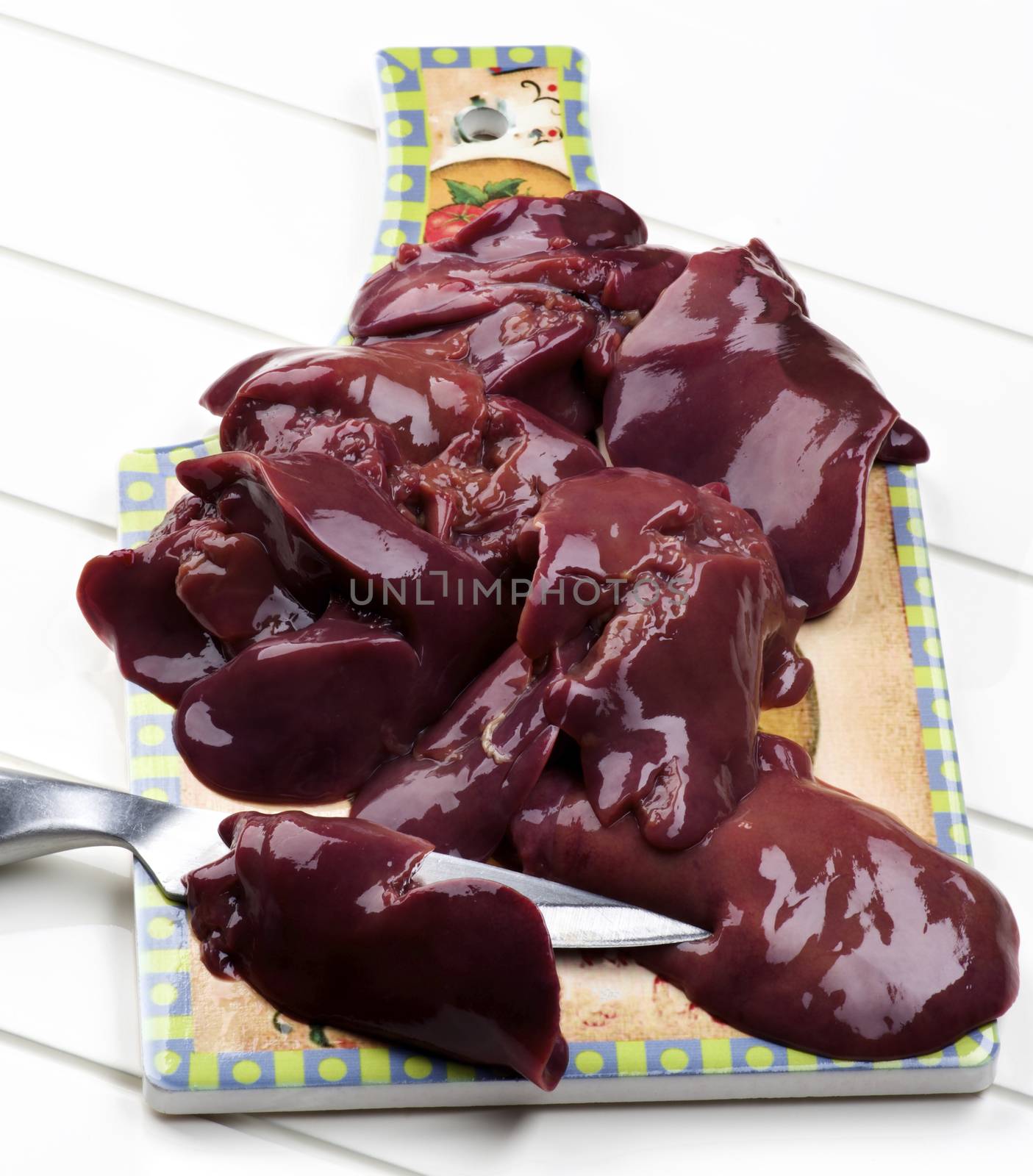 Fresh Raw Chicken Liver on Colorful Cutting Board with Kitchen Knife closeup on White Plank background