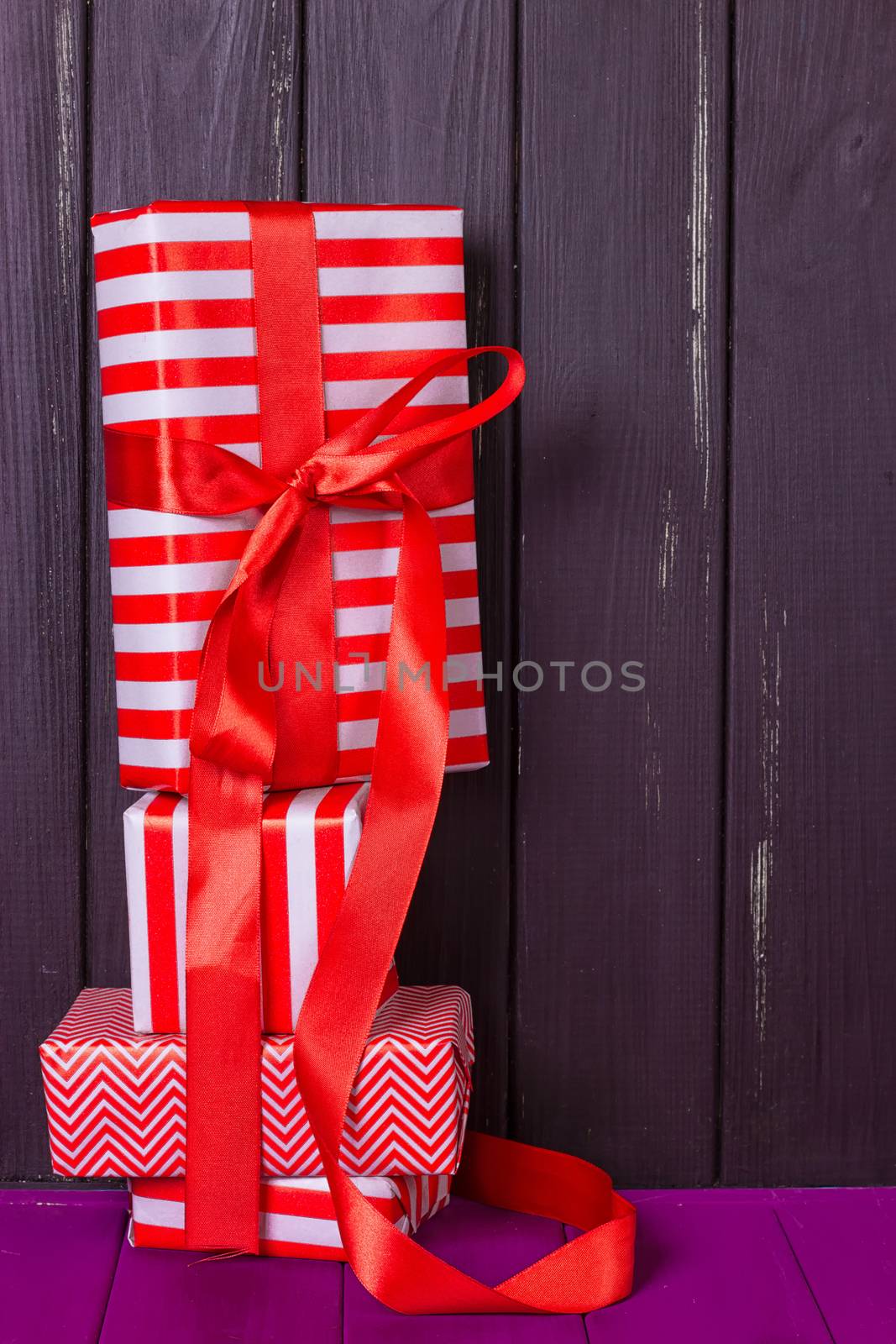 a slide of gifts in a red and white wrapper against a black wooden fence. Christmas presents