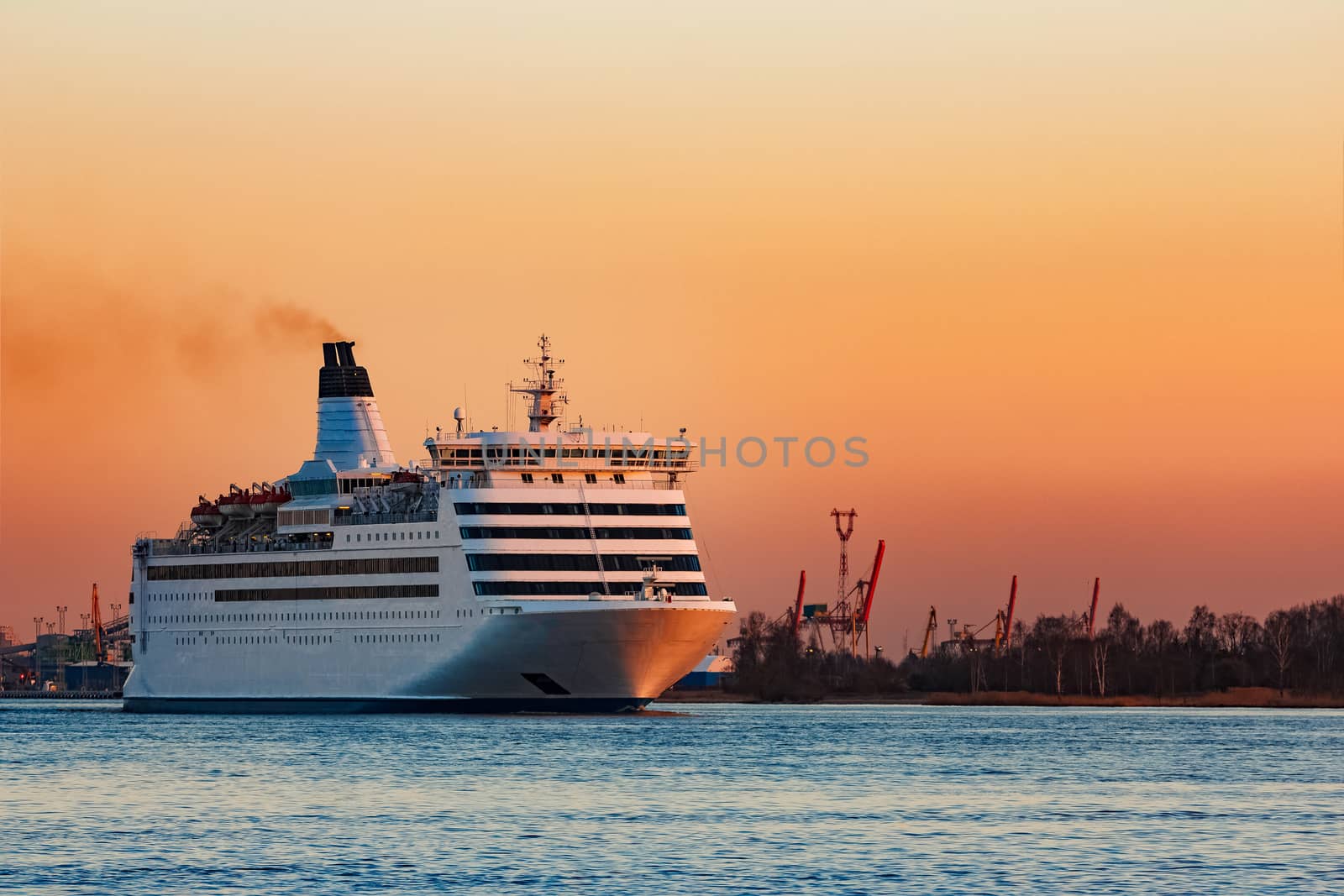 White passenger ship moving against the orange sunset sky