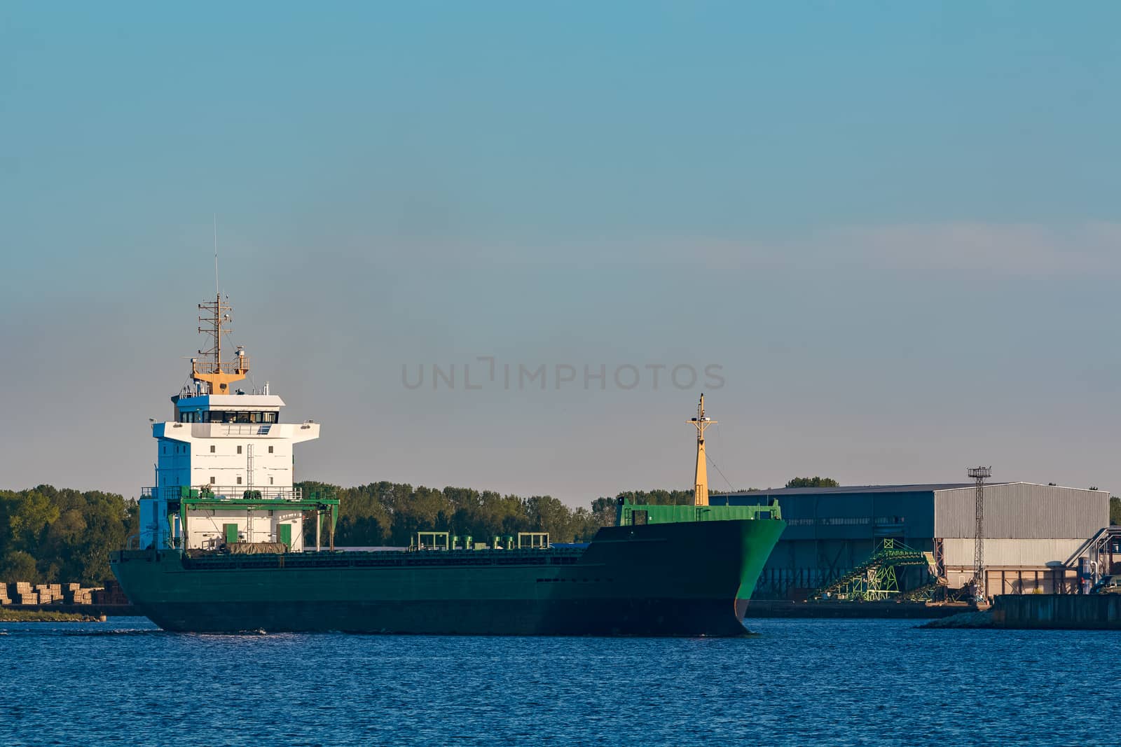 Green cargo ship leaves the port in a clear day