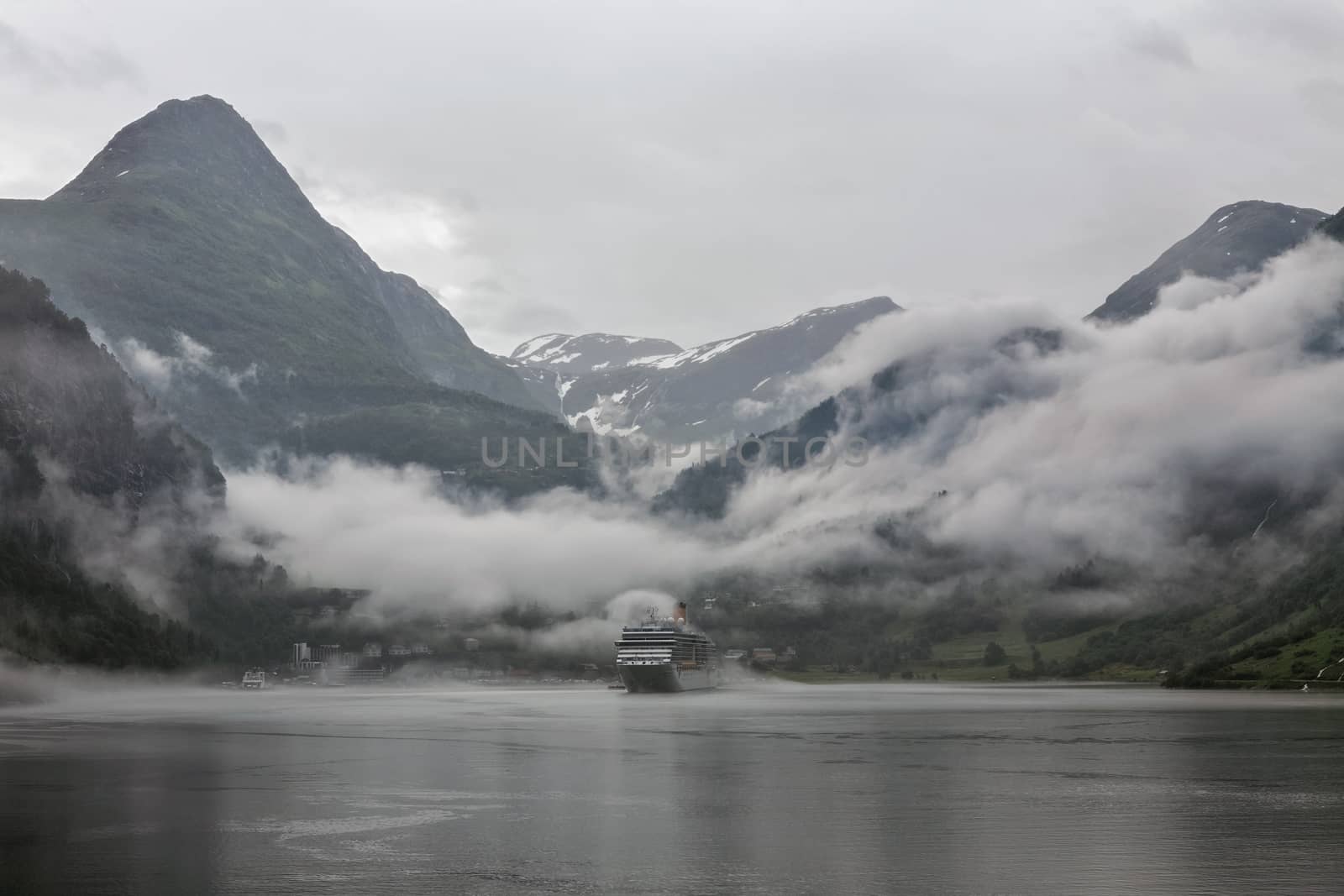 Cruise ship docked in Geiranger in a cloudy and foggy day, Norway