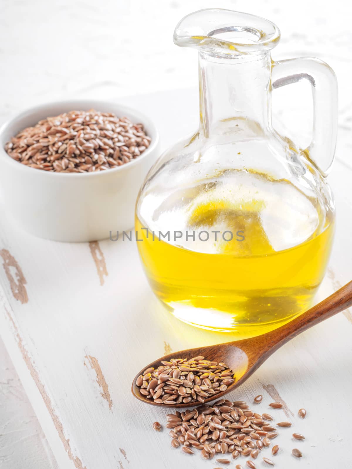 Brown flax seeds in spoon and flaxseed oil in glass bottle on white wooden background. Flax oil is rich in omega-3 fatty acid.