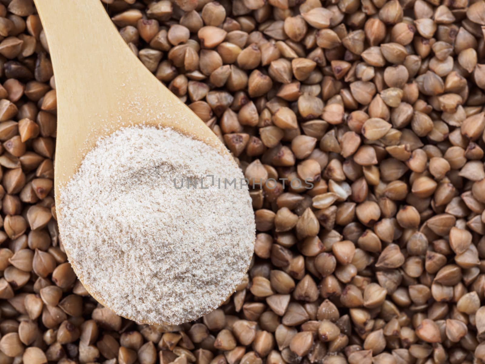 Buckwheat flour in wooden spoon and buckwheat grains. Whole-grain buckwheat flour on buckwheat grains background. Copy space. Top view or flat lay.