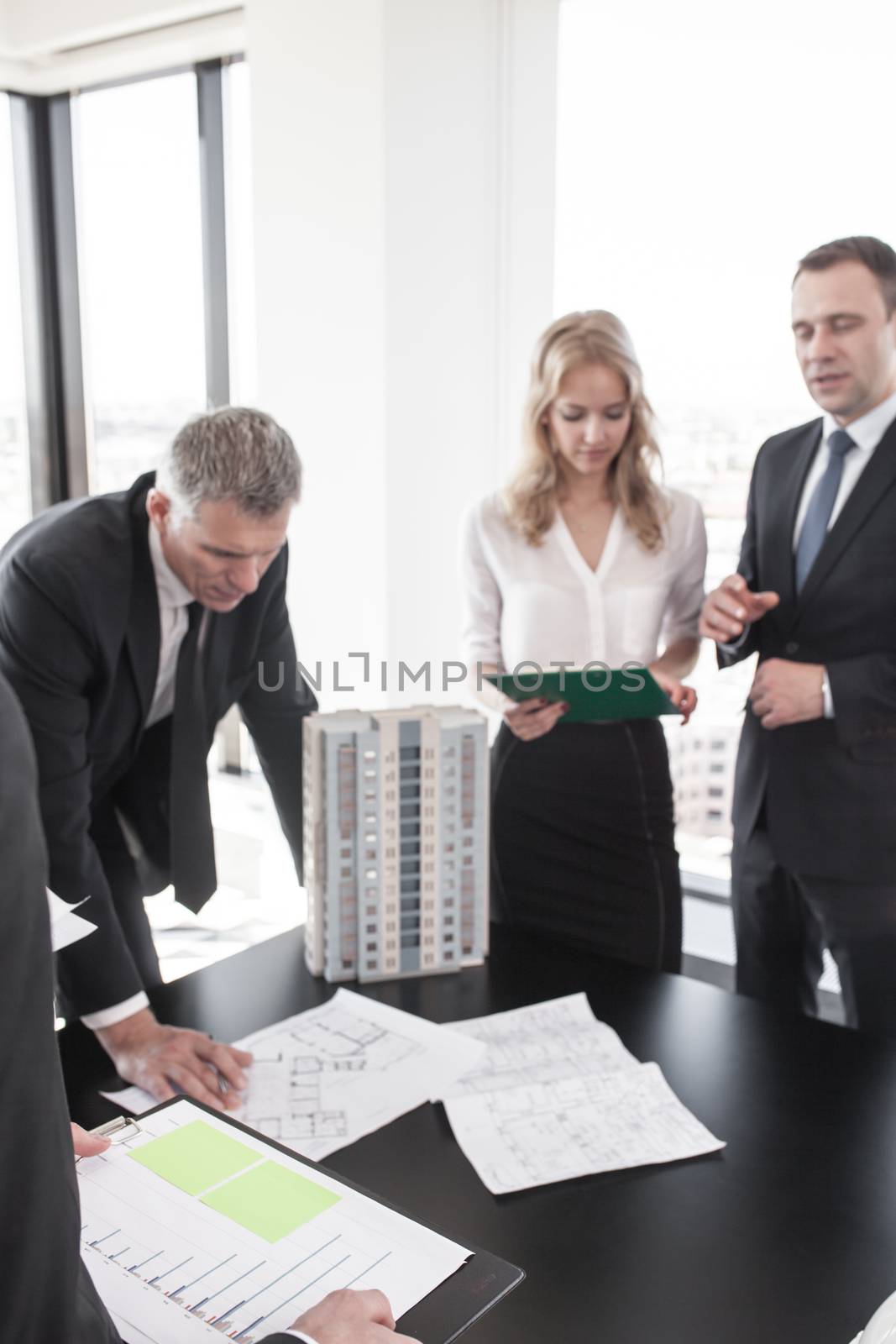 Business meeting of architects and investors looking at model of modern multi storey residential building house on table