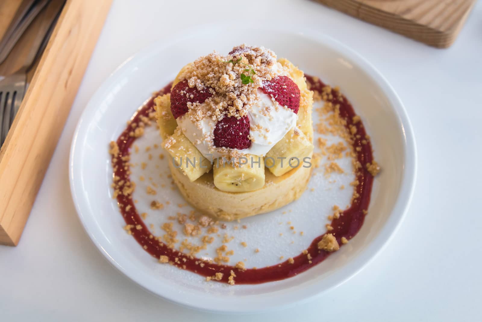 Hot cake with cream, strawberry, banana and cookie crumble on white dish