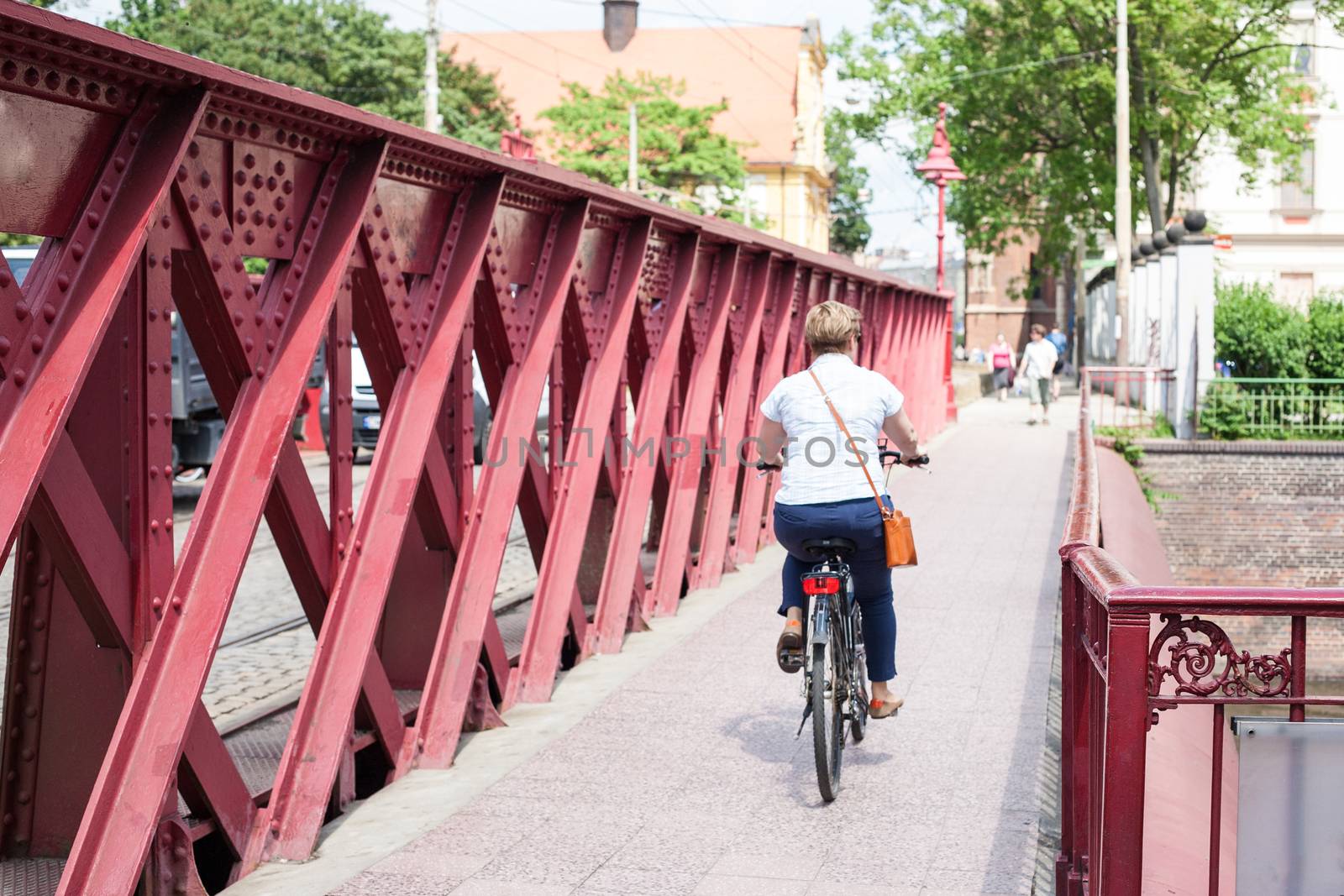 A woman crossing an old iron red bridge on a bicycle