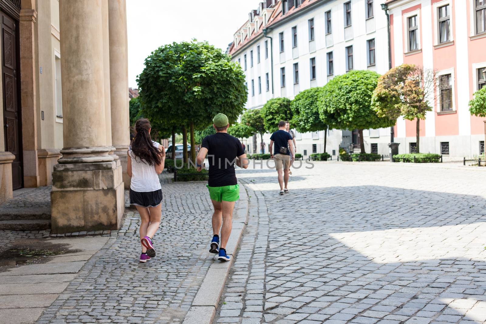 A young couple running along the historical side of the city of Wroclaw