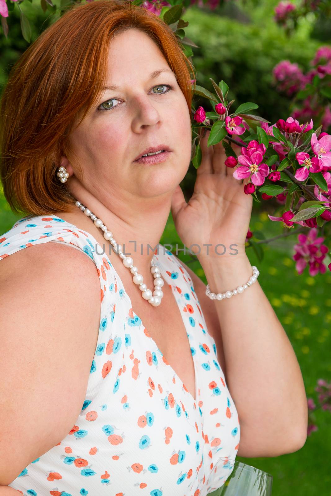 forty something brunette woman wearing a sun dress holding a branch of cherry tree in bloom