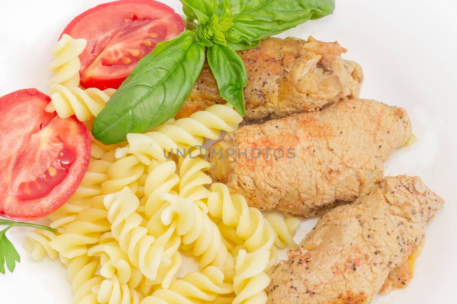 Top view of the braised stuffed meat roulades, spiral pasta and tomato, decorated with basil and parsley twigs closeup
