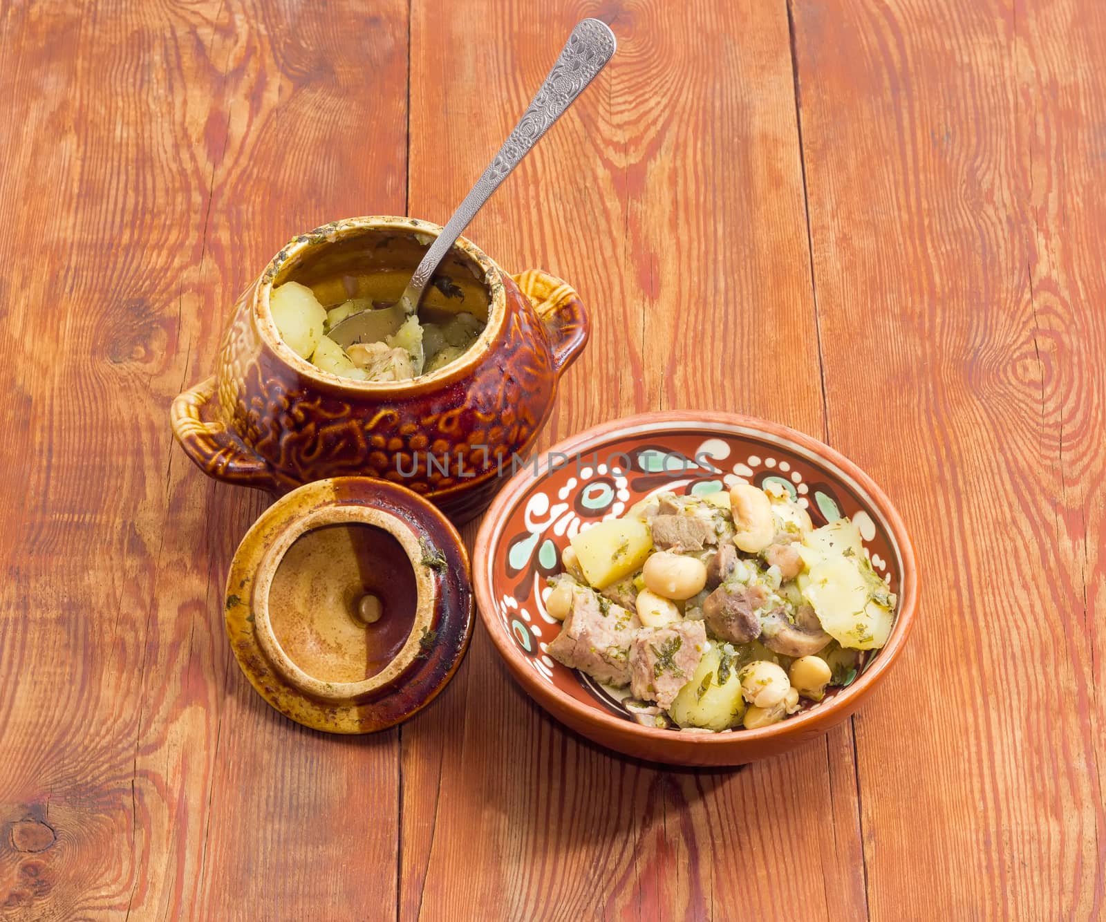 Ukrainian version of the dish Chanakhi in a clay bowl  - potatoes with meat, mushrooms and haricot beans roasted in a clay pot on a surface of an old wooden planks
