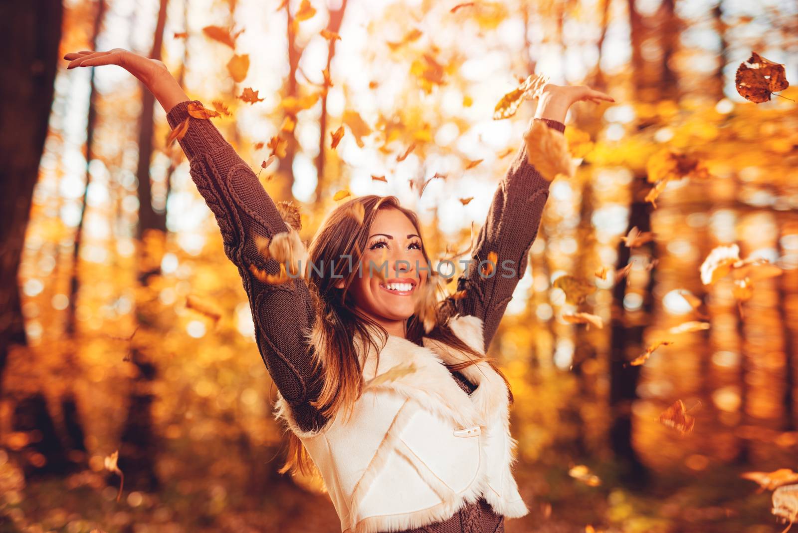 Cheerful young woman having fun in sunny forest in autumn colors.