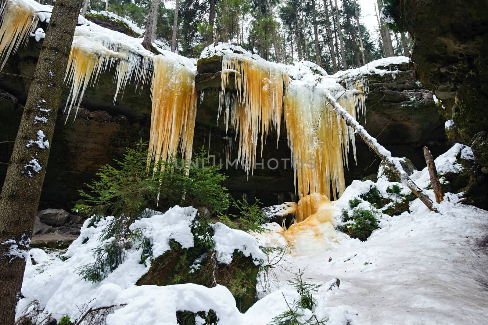 Frozen waterfalls on the rock, orange colored and snow