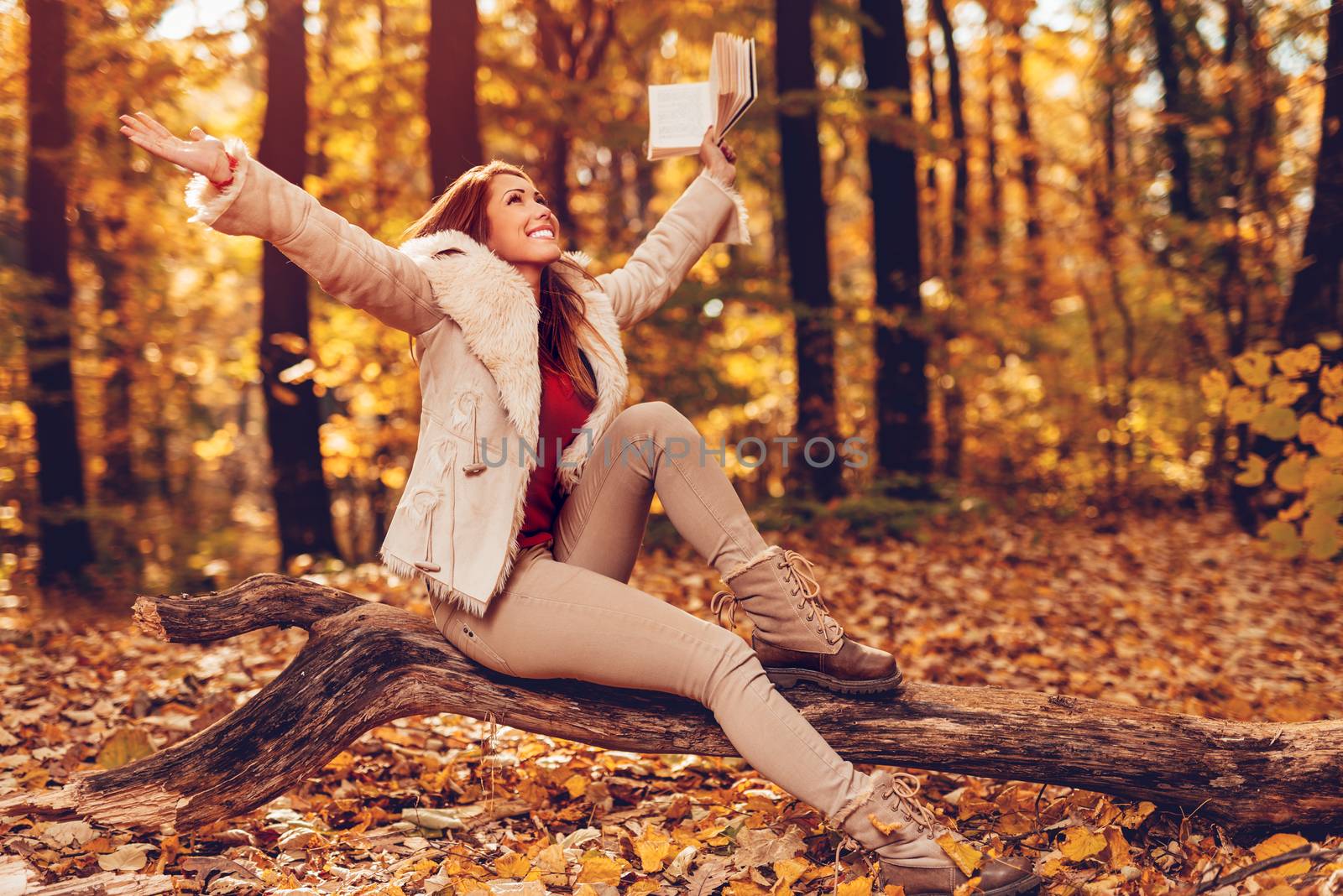 Beautiful young smiling woman holding book and having fun in sunny forest in autumn colors.