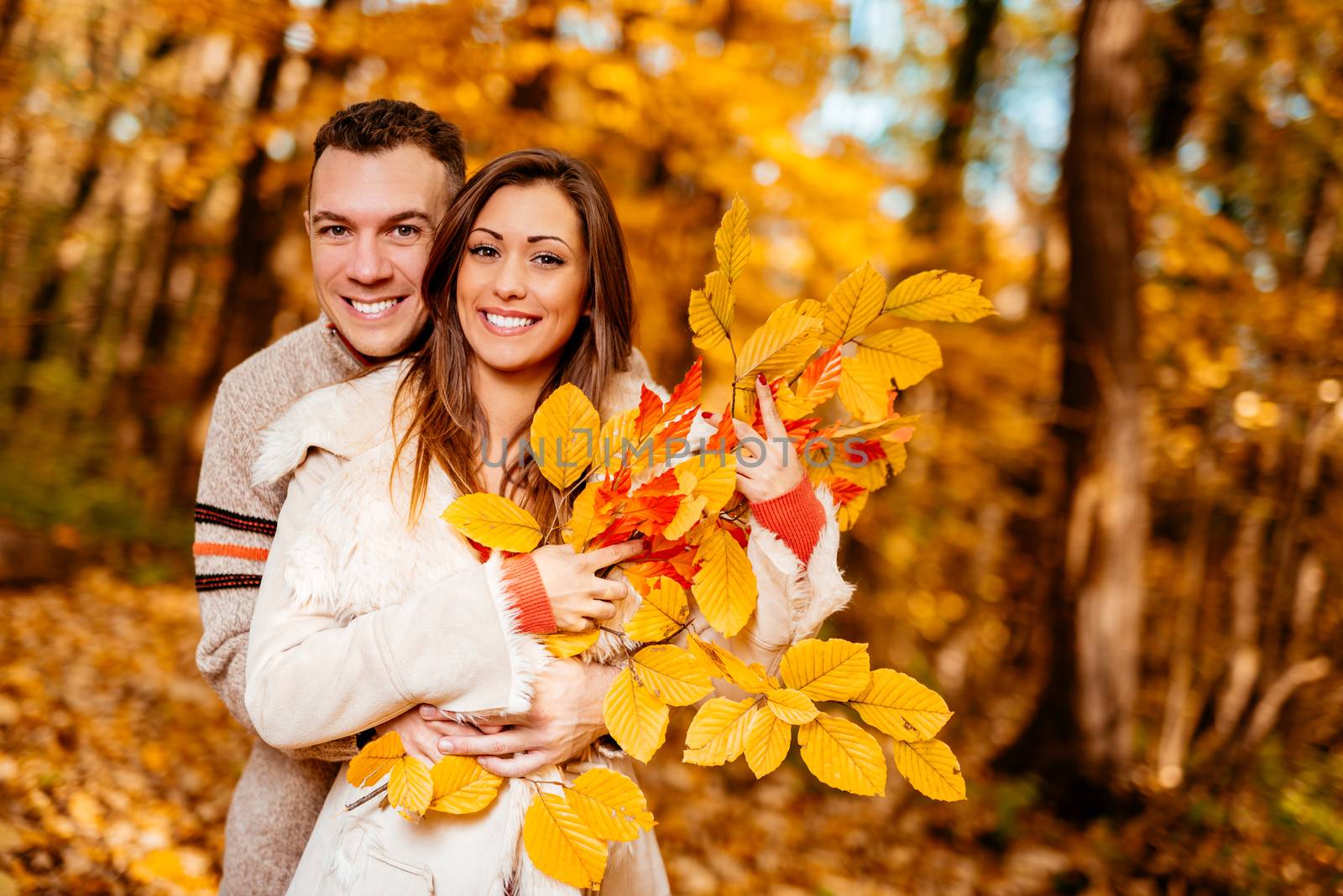 Portrait of a young smiling couple enjoying in sunny forest in autumn colors.