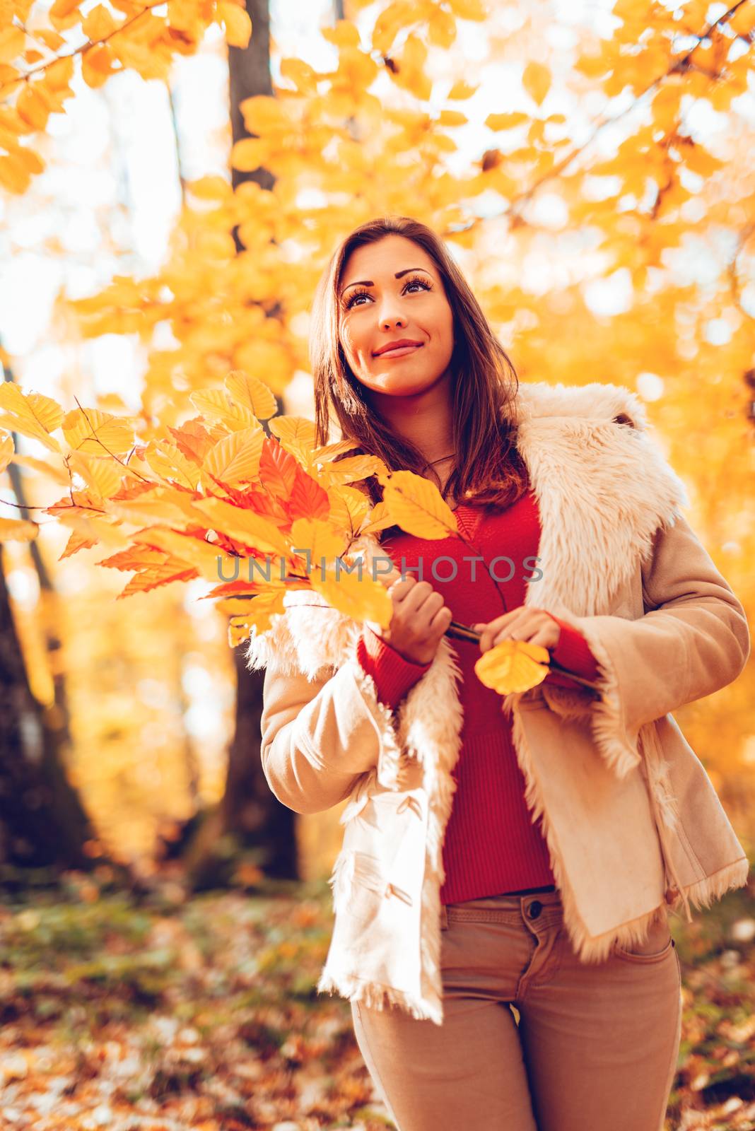 Beautiful smiling girl enjoying in forest in autumn. She is holding yellow leaves and thinking.