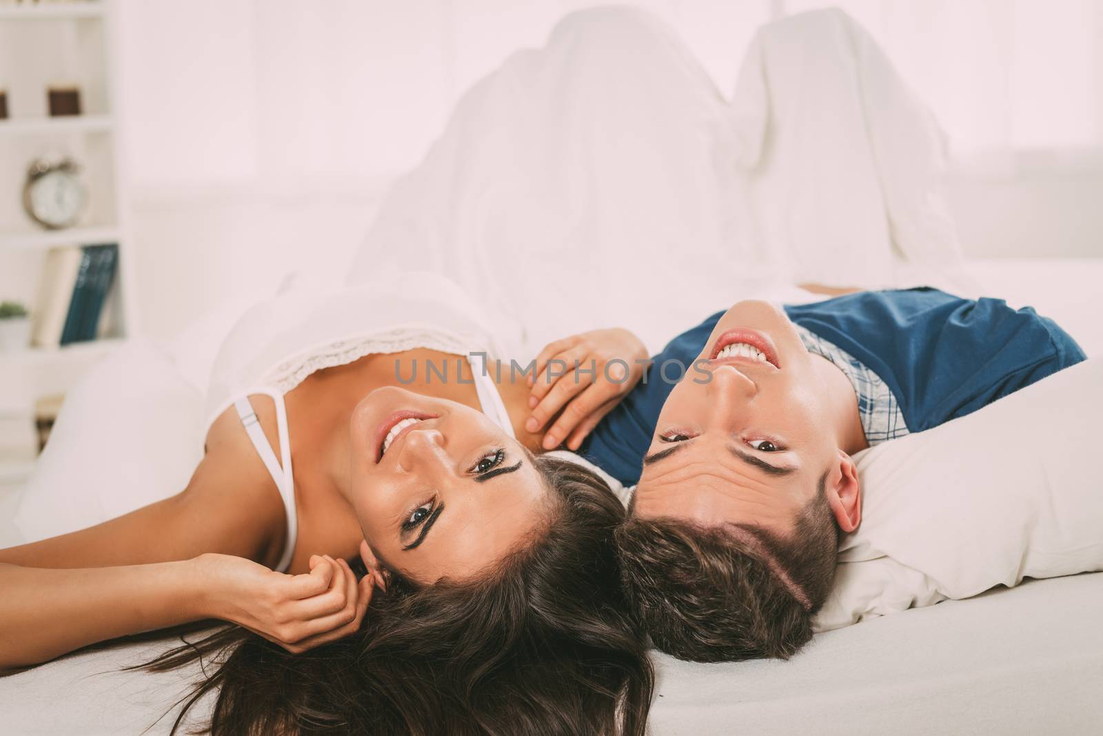 Beautiful young couple relaxing and having fun in the bed. Looking at camera.