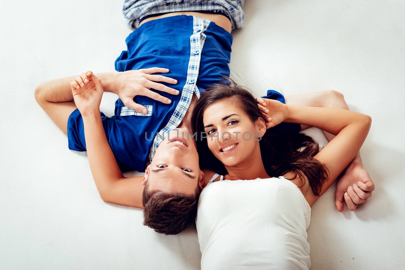 Top view of a beautiful smiling couple relaxing in the bed. Looking at camera.