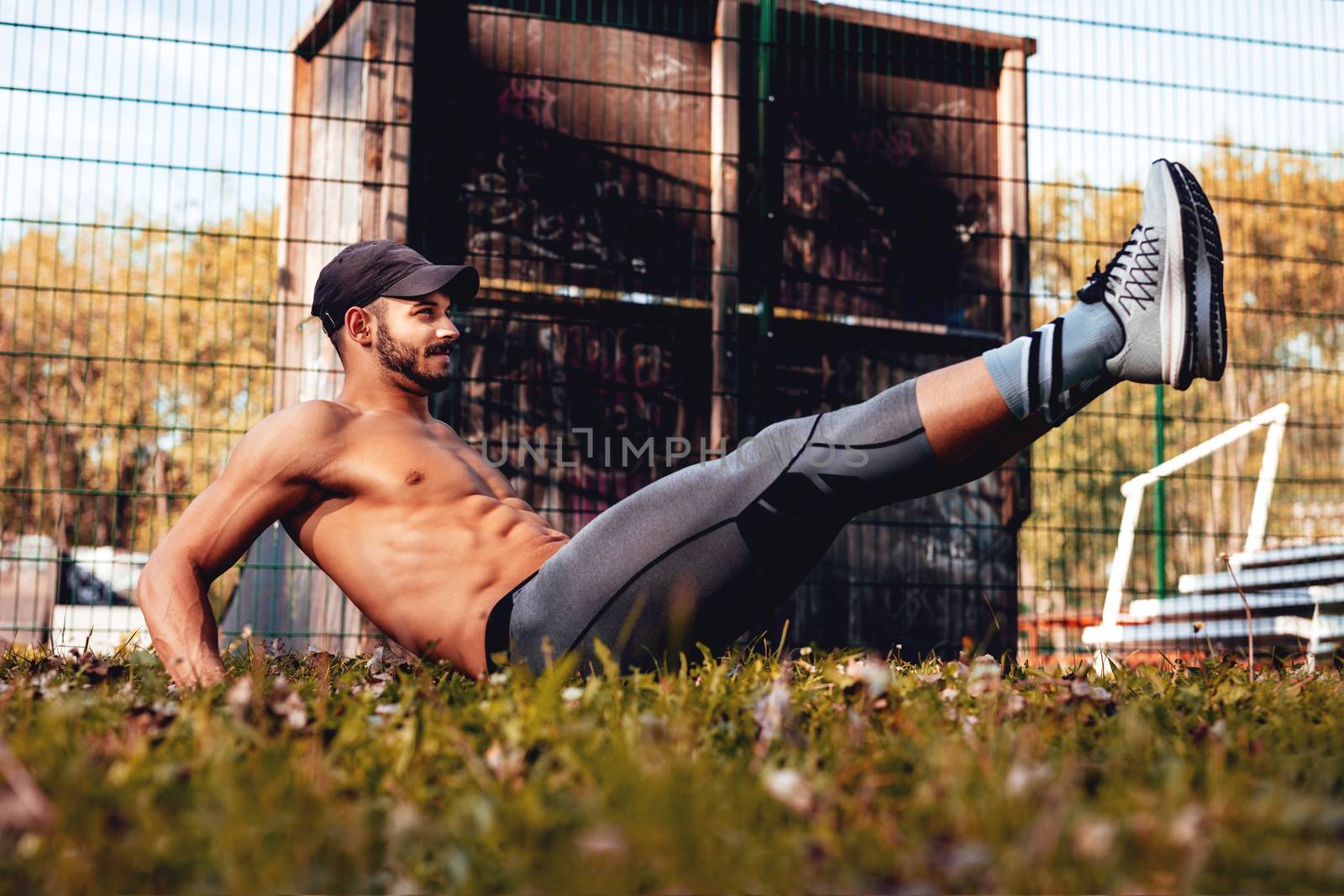 Young urban muscular sportsman doing sit-ups exercise in the park.