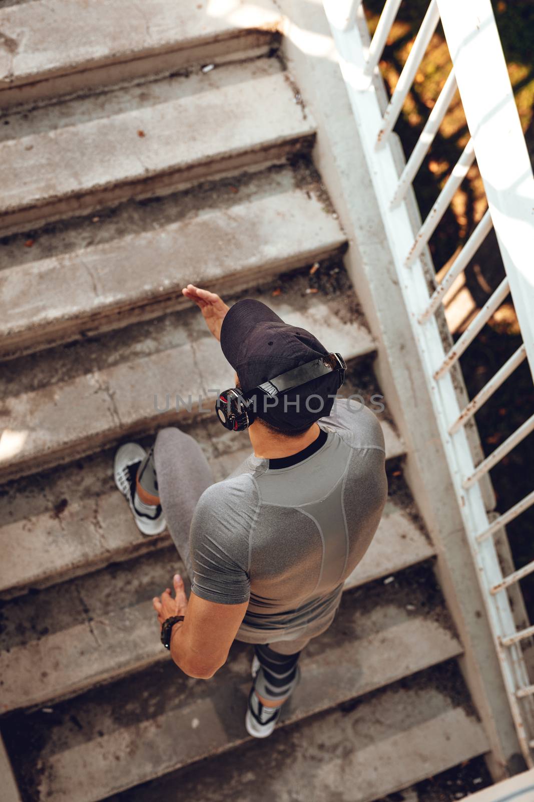 Young muscular sportsman with headphones jogging up the stairs at the bridge. 