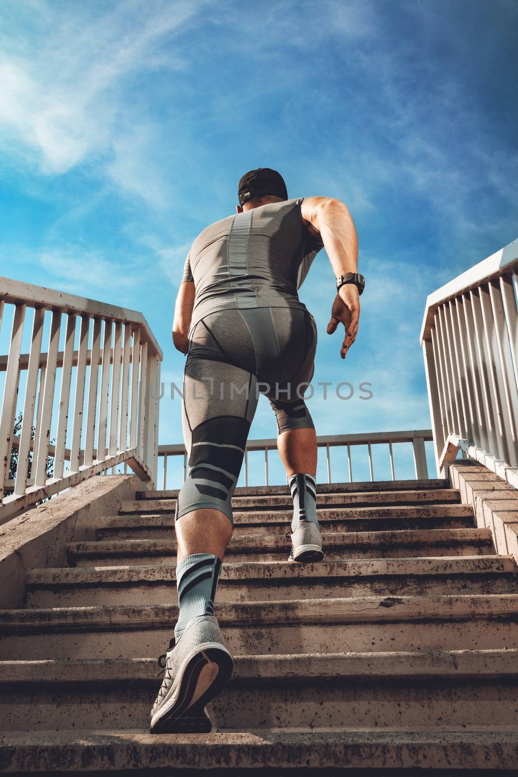 Young muscular sportsman running up the stairs at the bridge. Rear view. 