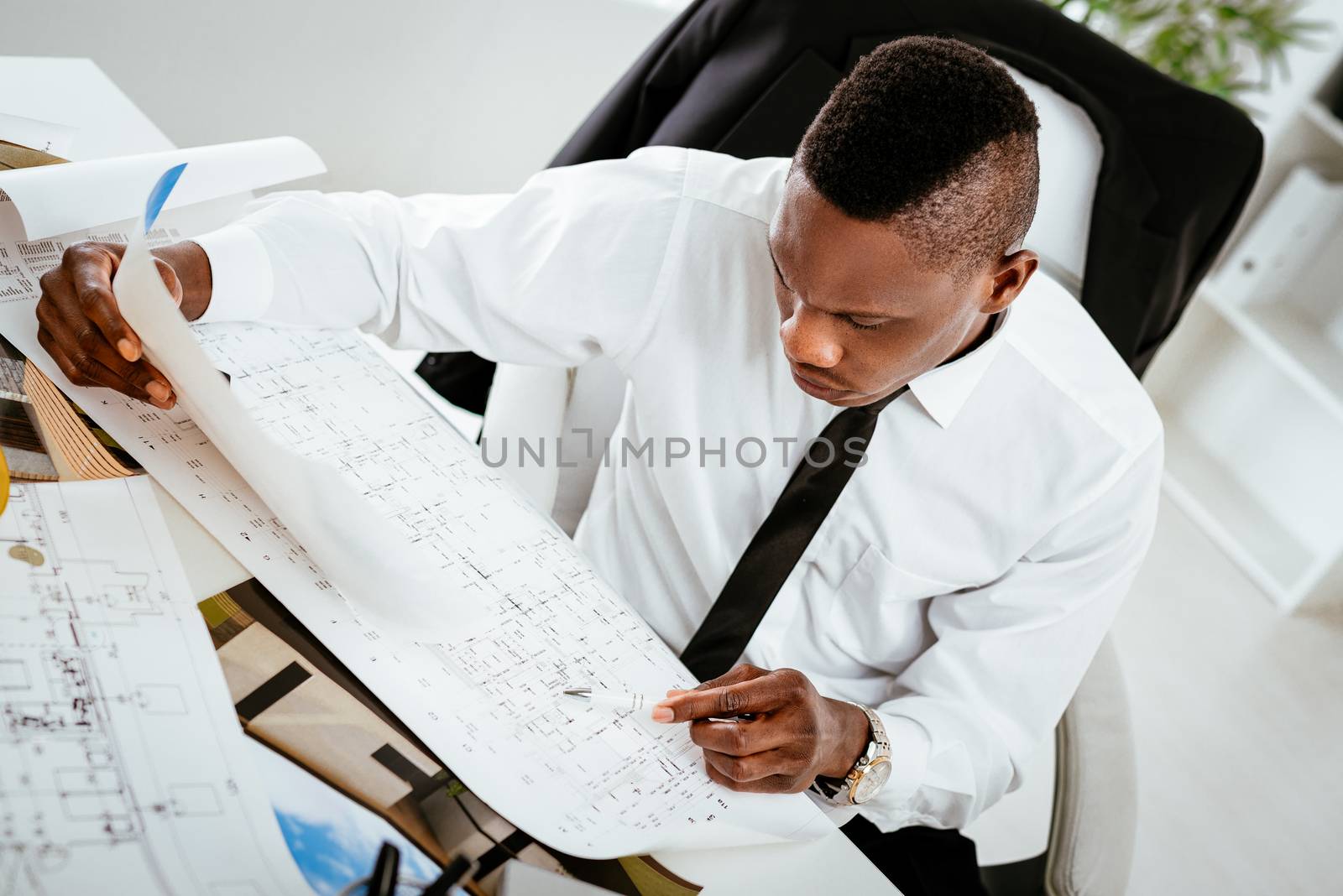 Pensive African construction engineer analyzing blueprint at desk in office. 