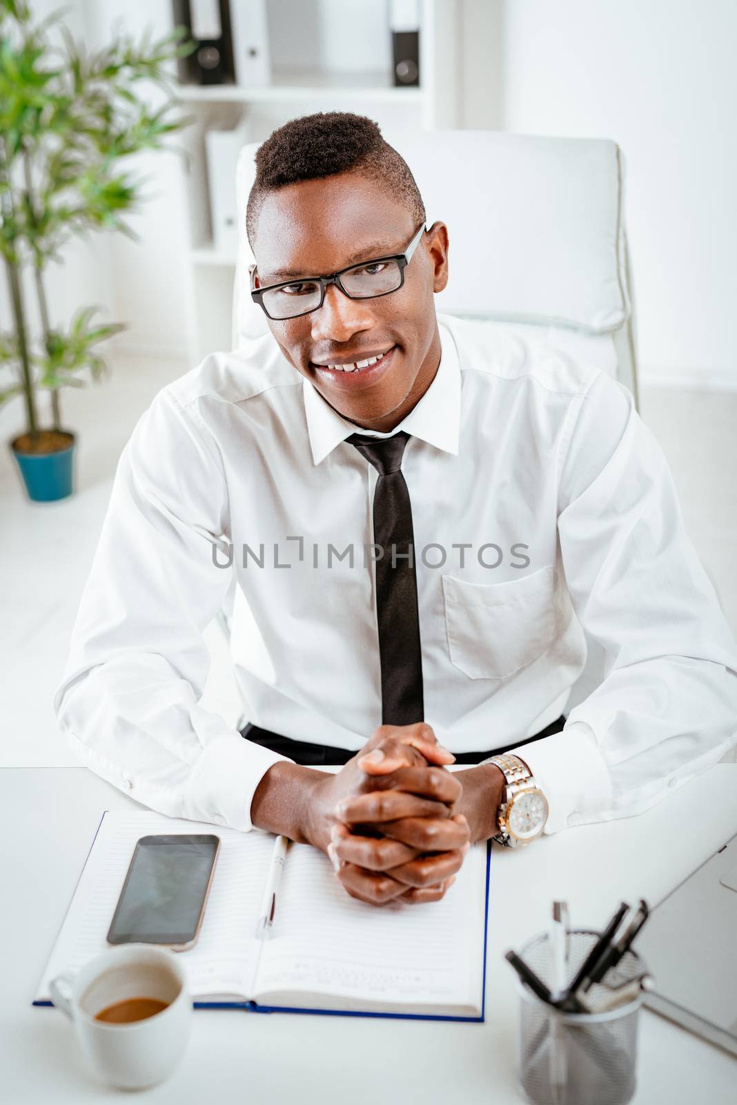 African smiling businessman with glasses sitting in the office and looking at camera.