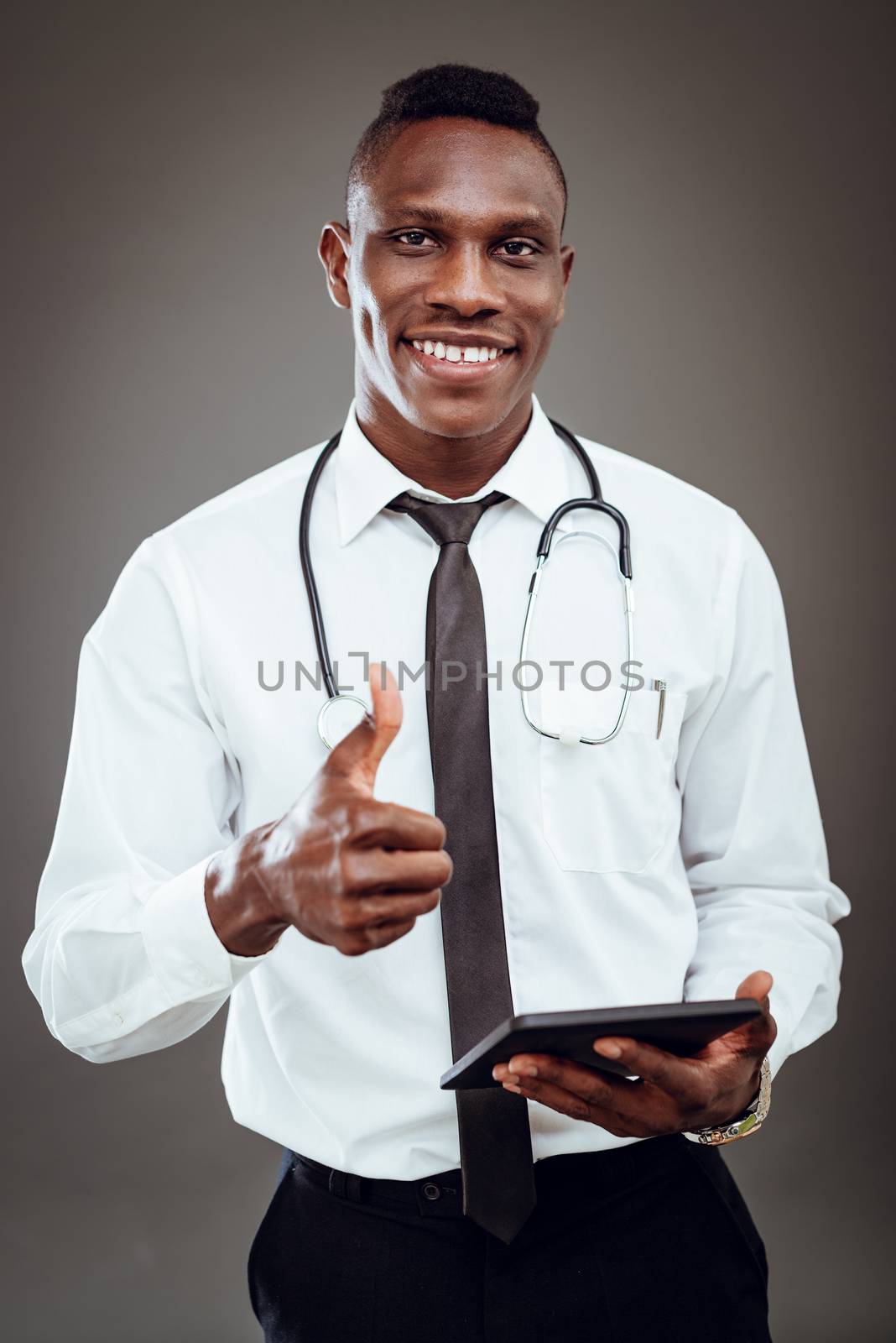 African smiling doctor with stethoscope standing and using digital tablet. Looking at camera.