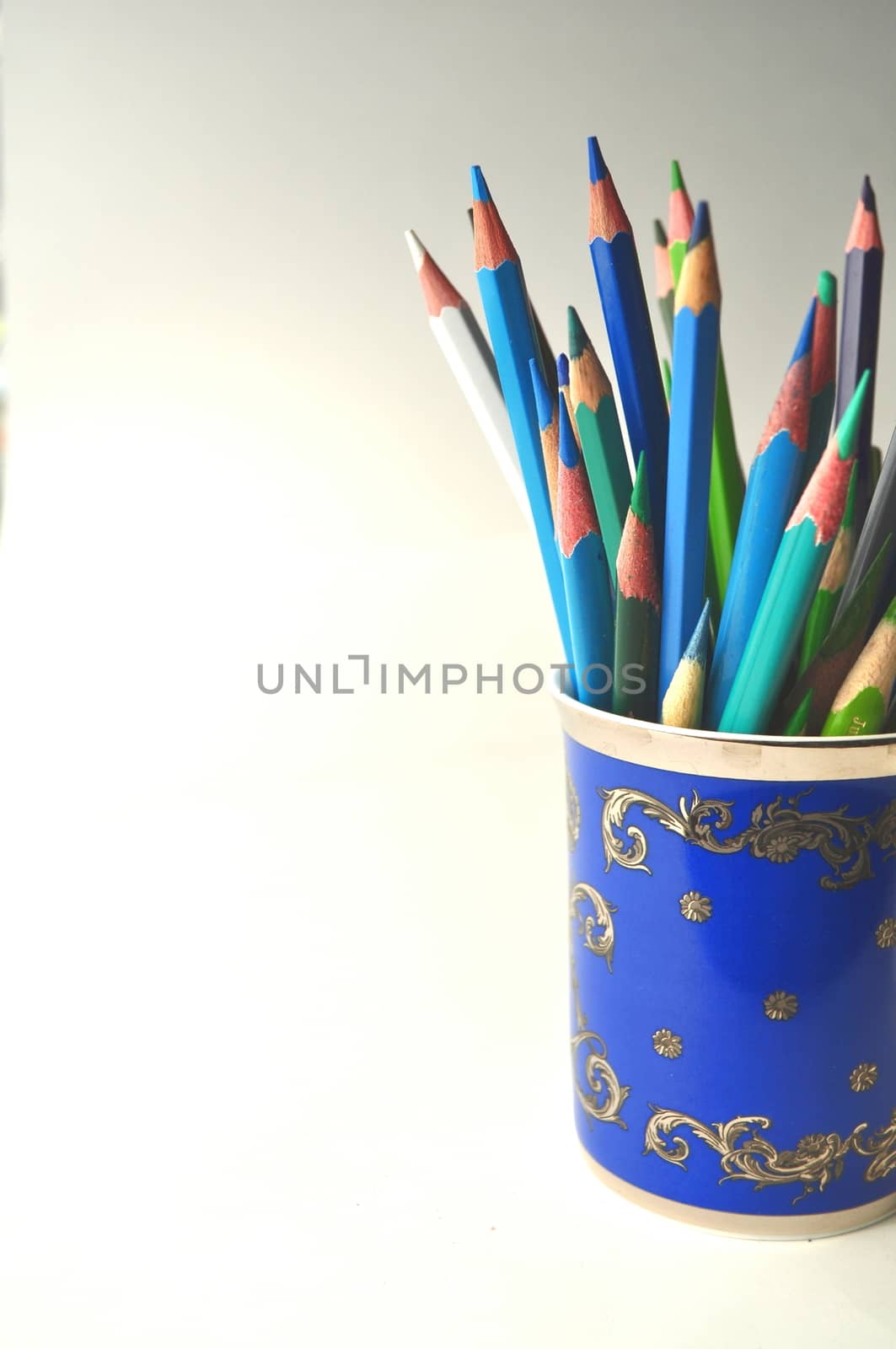 Blue porcelain cup with colorful pencils on grey, white and blue background with copy space