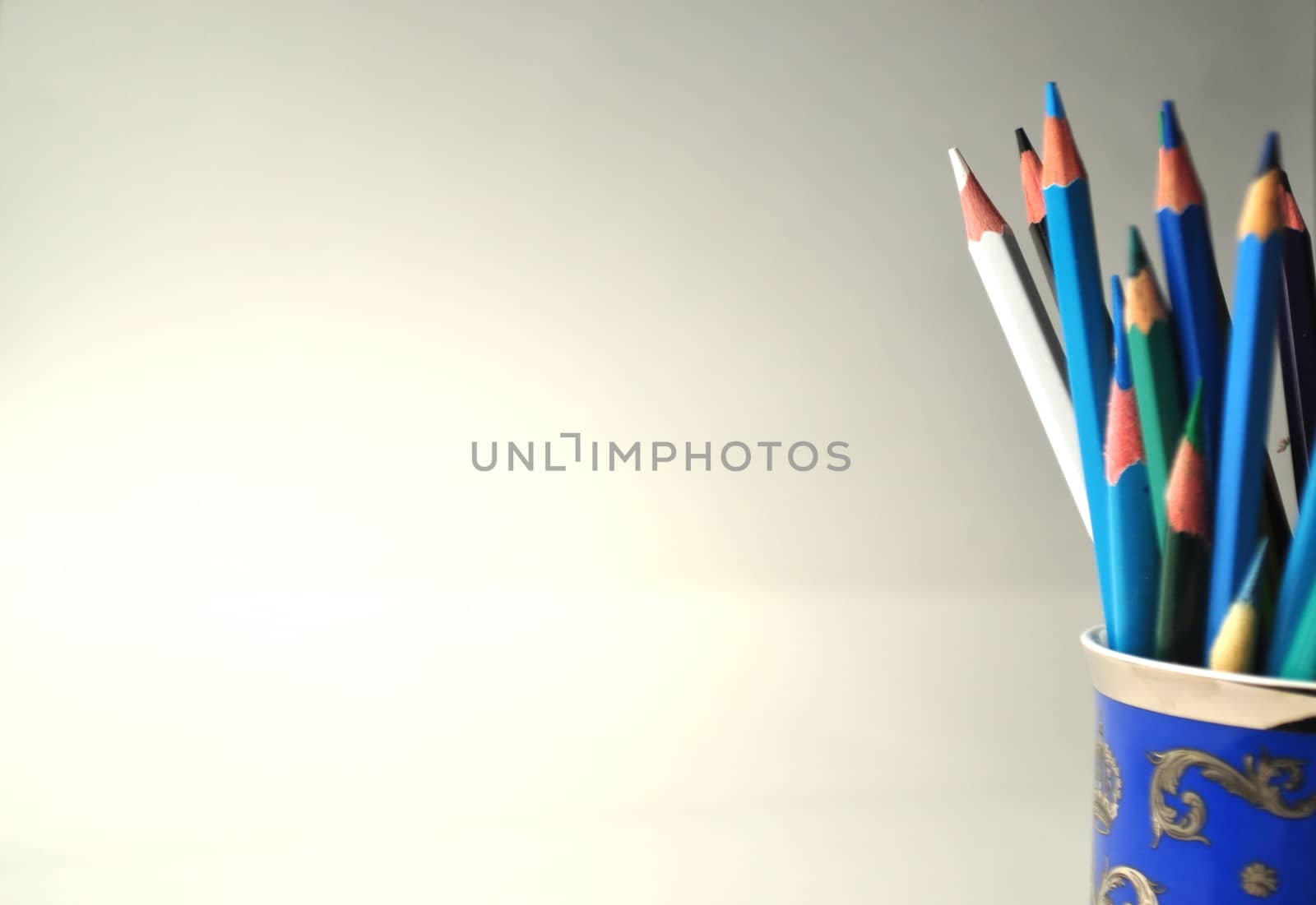 Blue porcelain cup with colorful pencils on grey, white and blue background with copy space