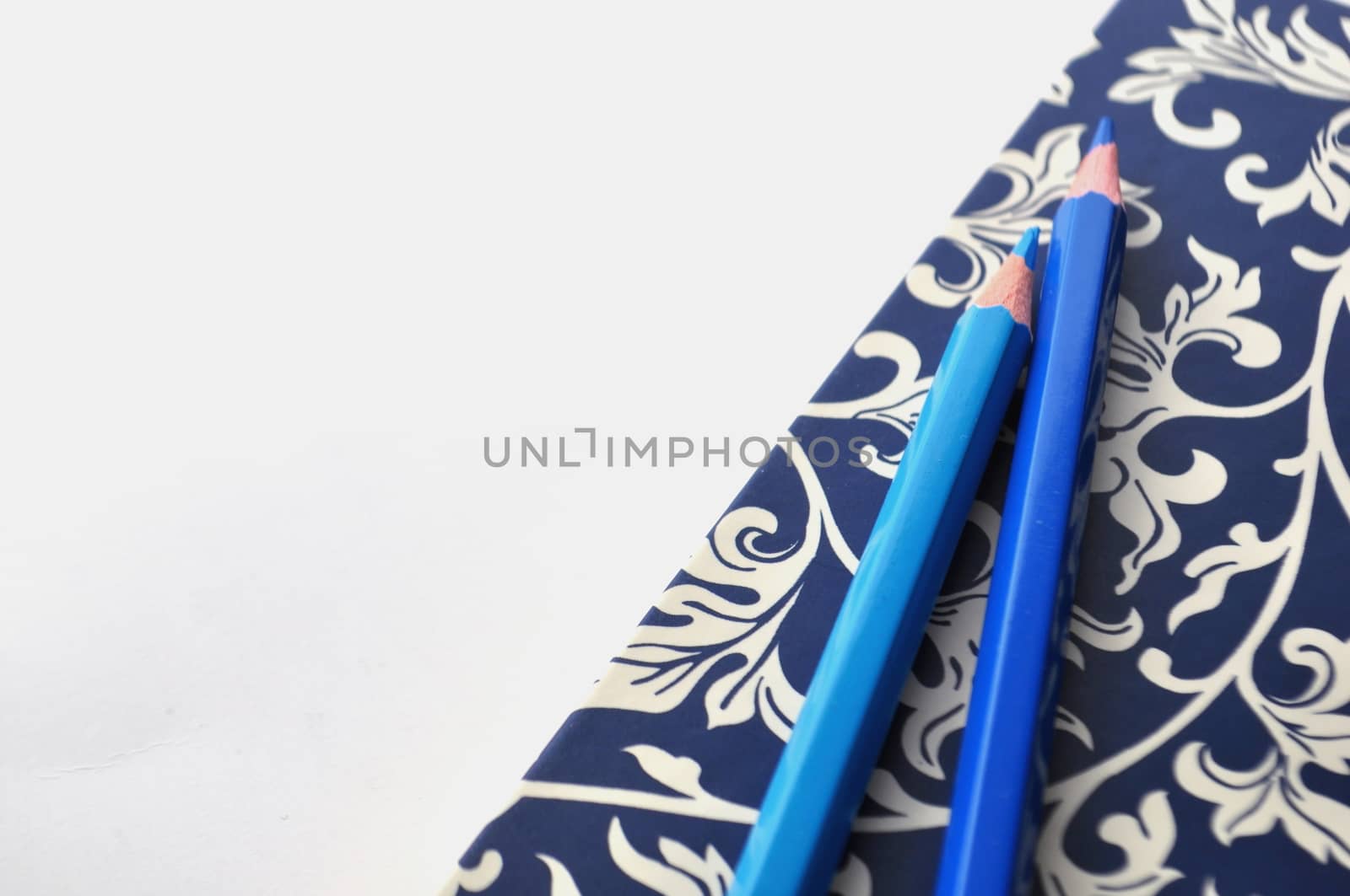 Floral notebook with blue pencils and white and blue background with copy space