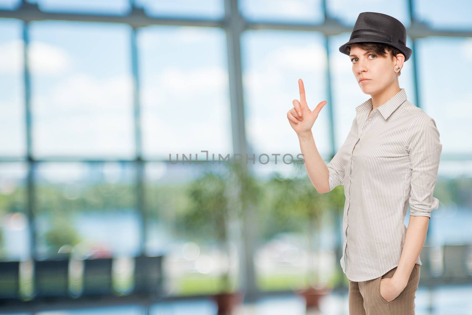 serious girl holds fingers pistol and wears a black hat in the office