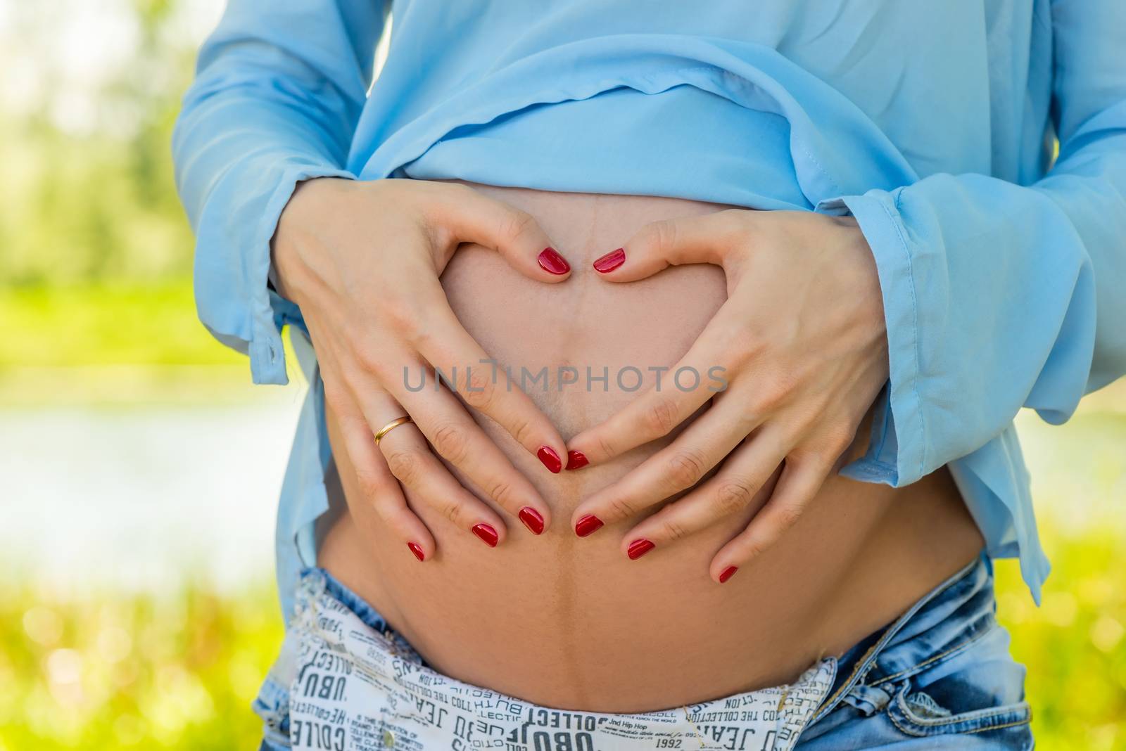 Hands in the shape of a heart on the belly of a pregnant woman close-up