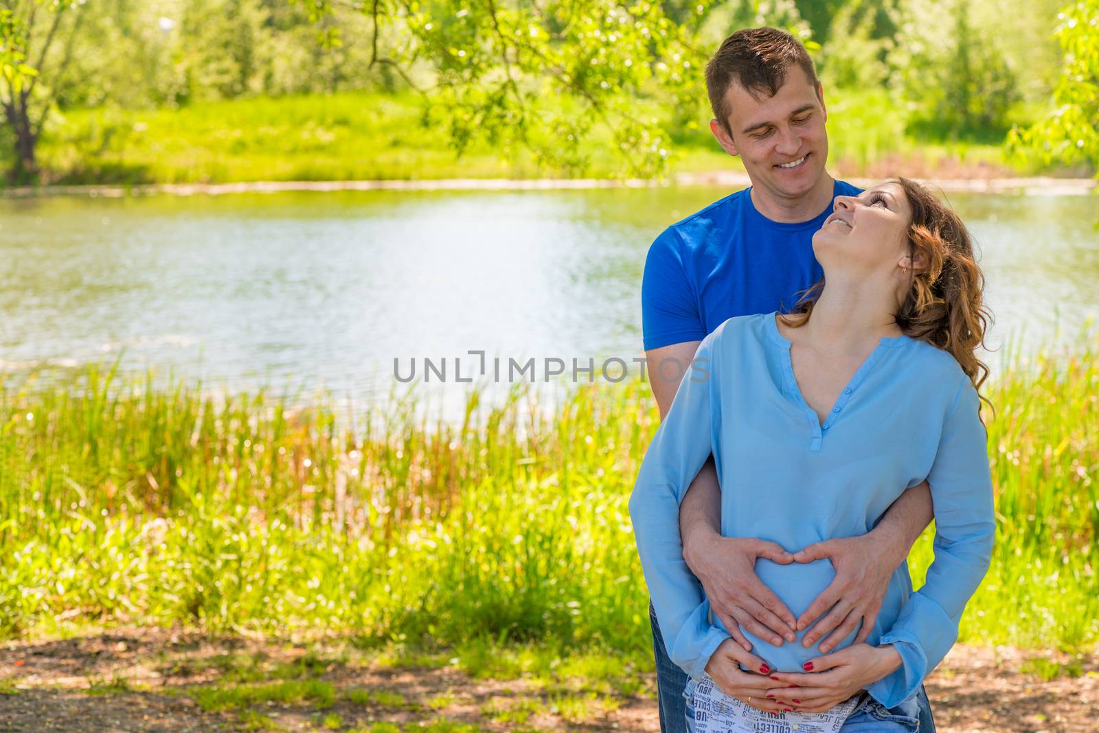 Pregnant woman and her husband in a park near the water hugging