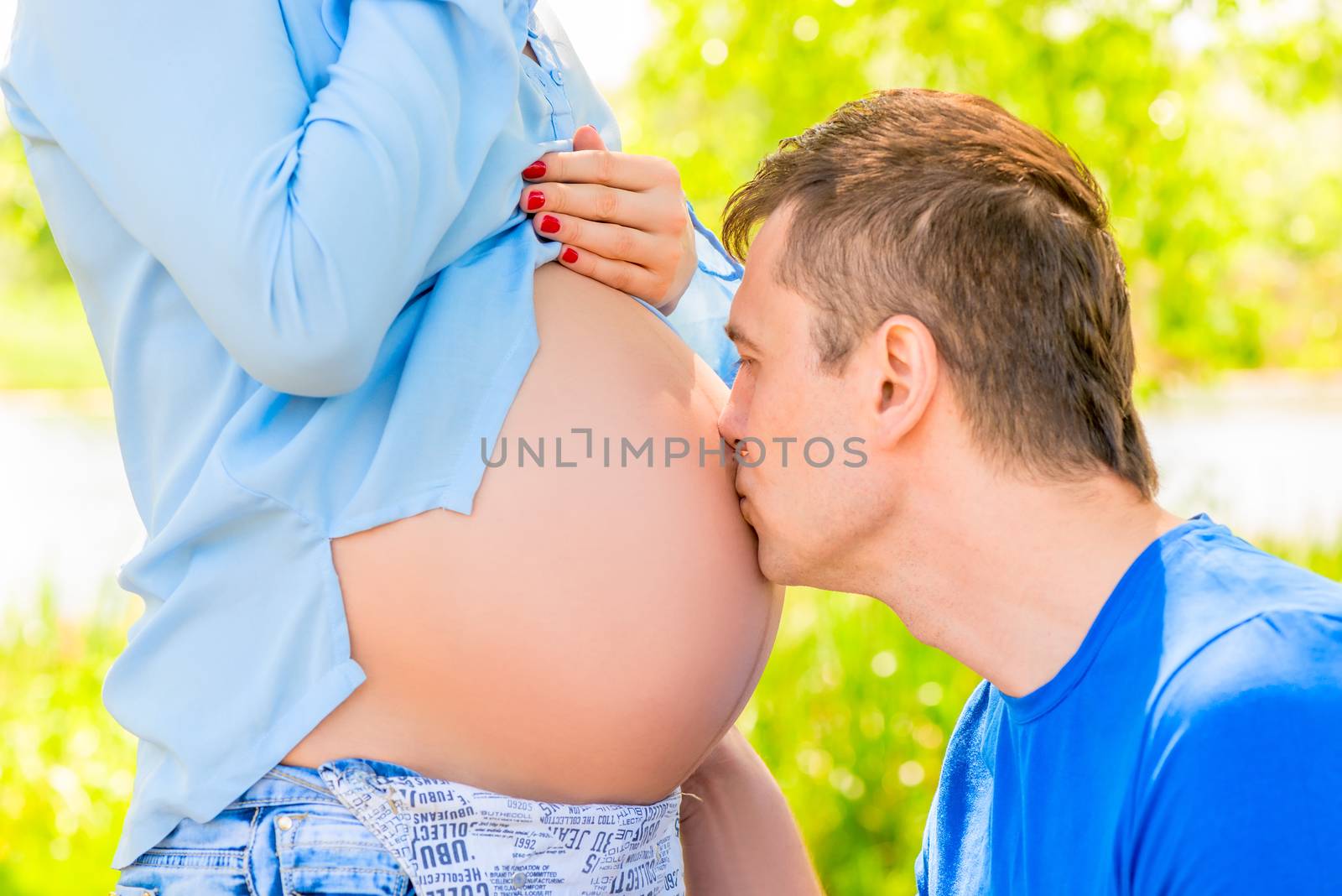 Happy man kisses the belly of his pregnant wife in the park by kosmsos111