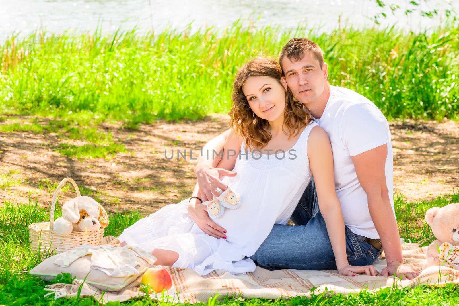 Picnic near the lake, young pregnant couple on a plaid