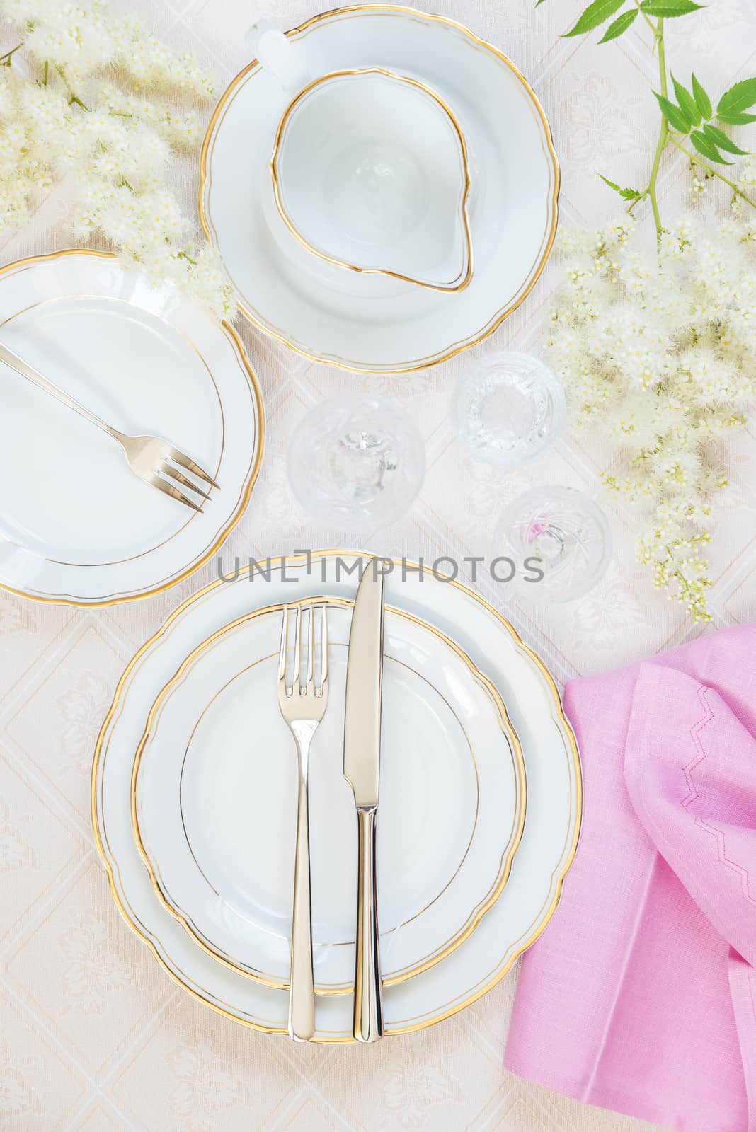 Top view of the beautifully decorated table with white plates, crystal glasses, pink linen napkin, cutlery and flowers on luxurious tablecloths