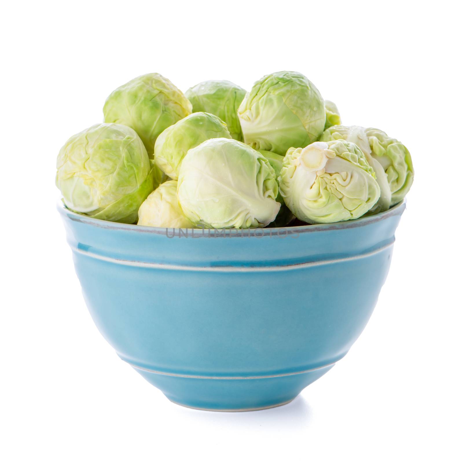 Fresh brussels sprouts on blue ceramic bowl isolated on white background.
