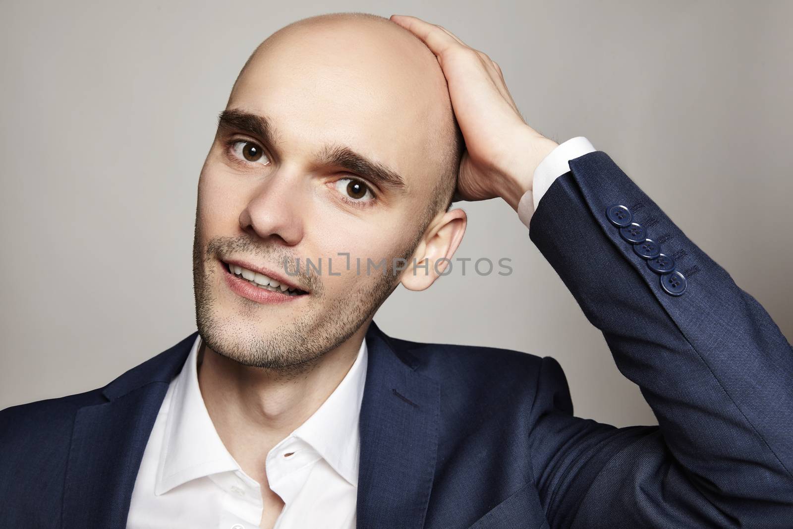 Close-up portrait of a handsome bald man stroking his head. He is smiling. Gray background. Horizontal.