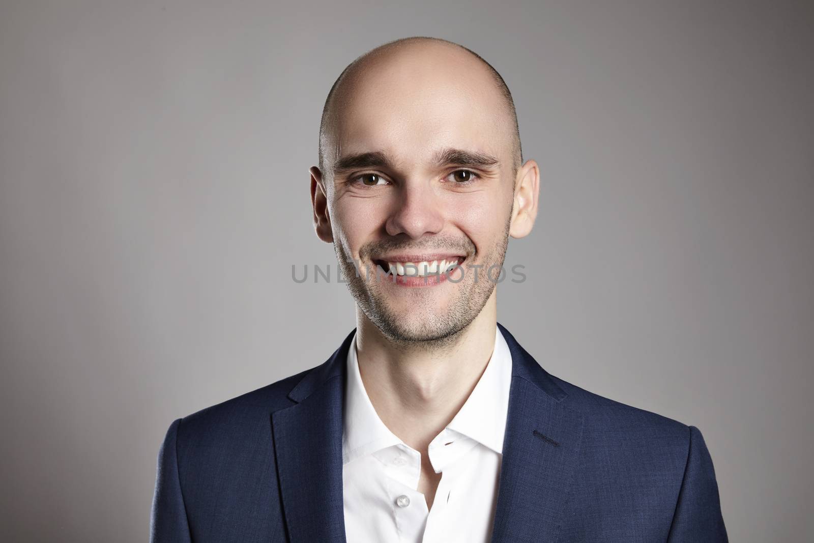 Studio shot of young man looking at the camera. Horizontal format, he is smiling, he is wearing a black jacket.