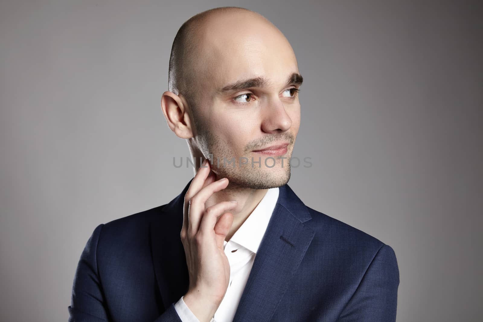 Portrait of a young man stroking his chin. Headshot on gray background.