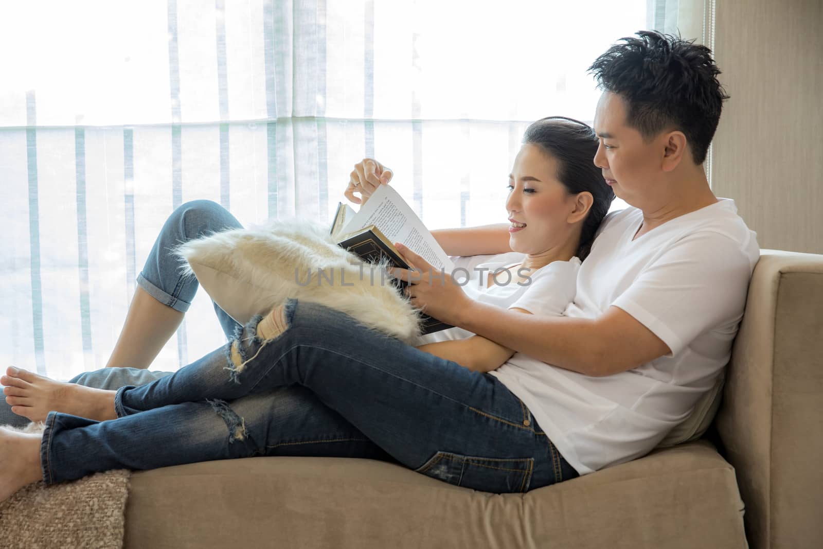 Young Couples reading book tohether in living room of contemporary house for lifestyle concept