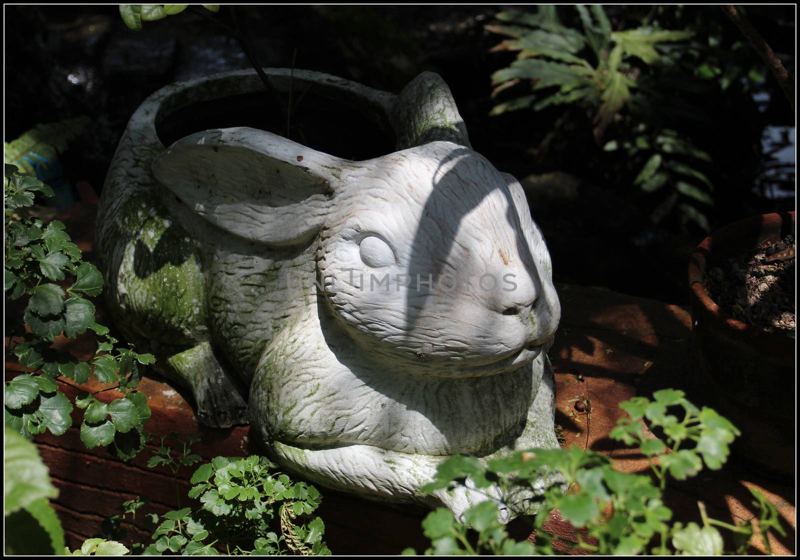 Gypsum figure of a hare in the shade, surrounded by foliage and green grass